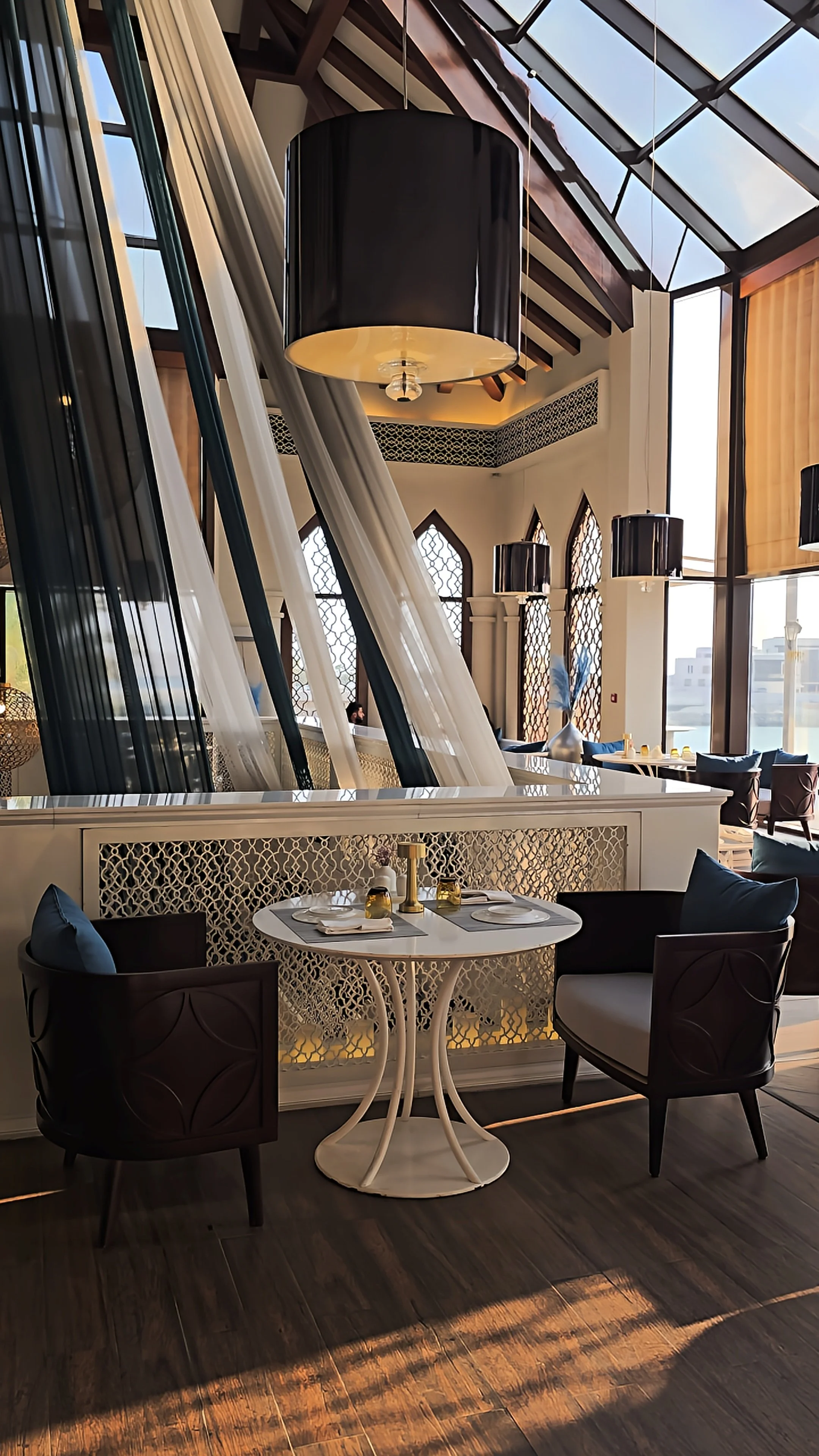Elegant restaurant interior featuring floor-to-ceiling windows, high ceilings, decorative screens, and modern dining furniture