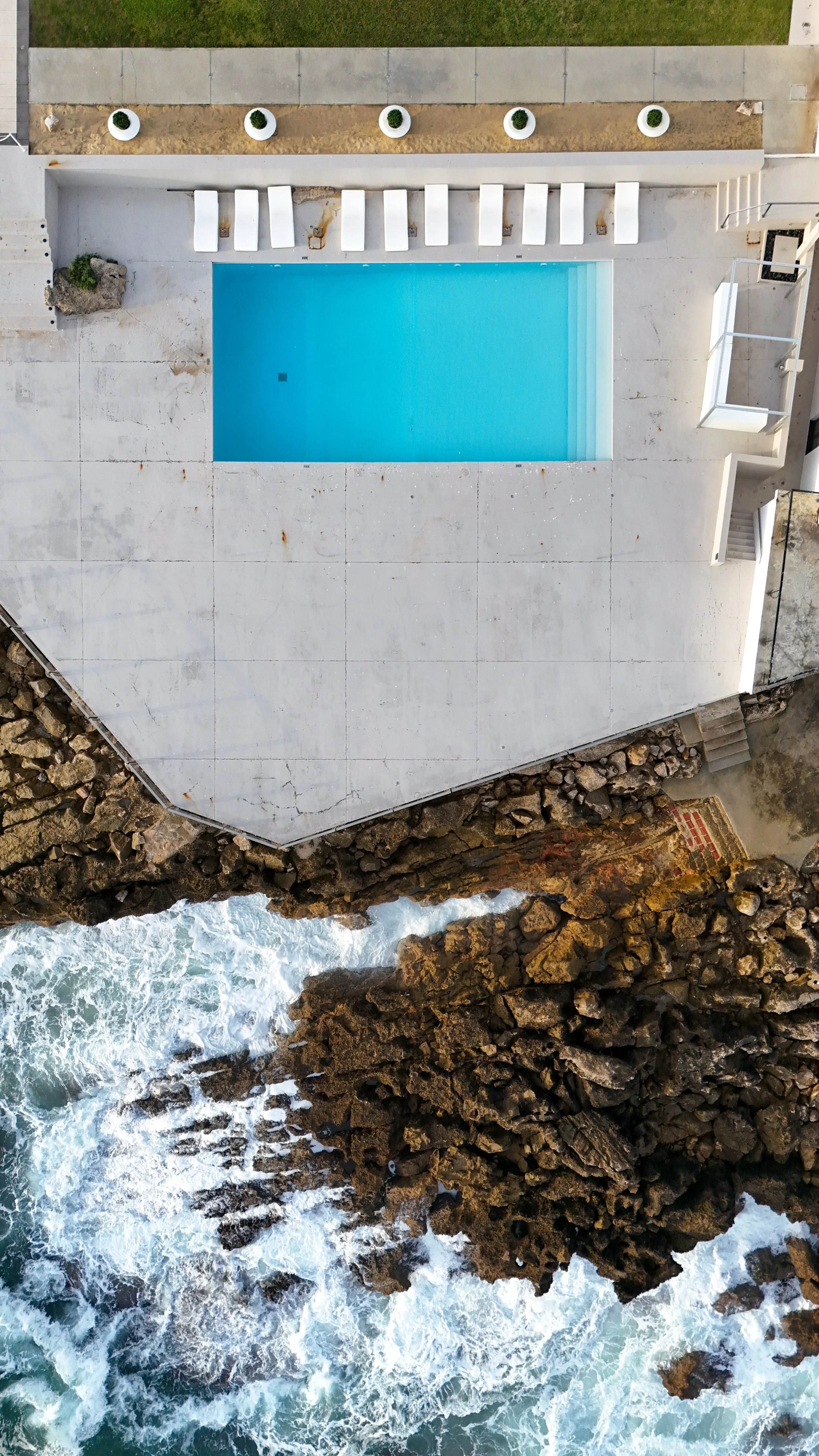 Aerial view of the oceanfront infinity pool set above Cascais’ dramatic rocky coastline