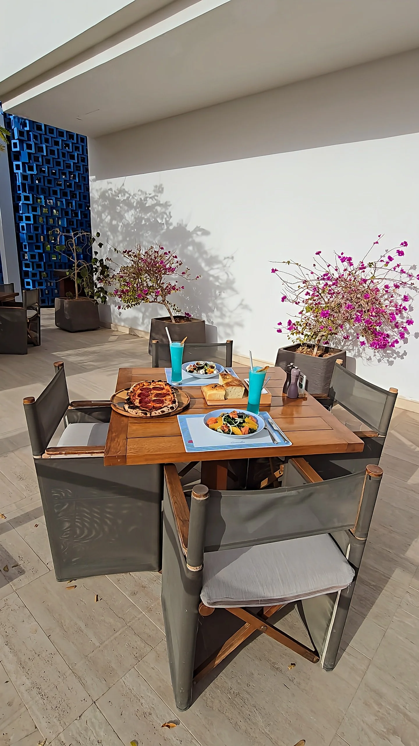 Outdoor terrace dining with pizza, fresh salads, and blue cocktails beside blooming bougainvillea, Hyatt Regency Aqaba Ayla Resort – Aqaba, Jordan.