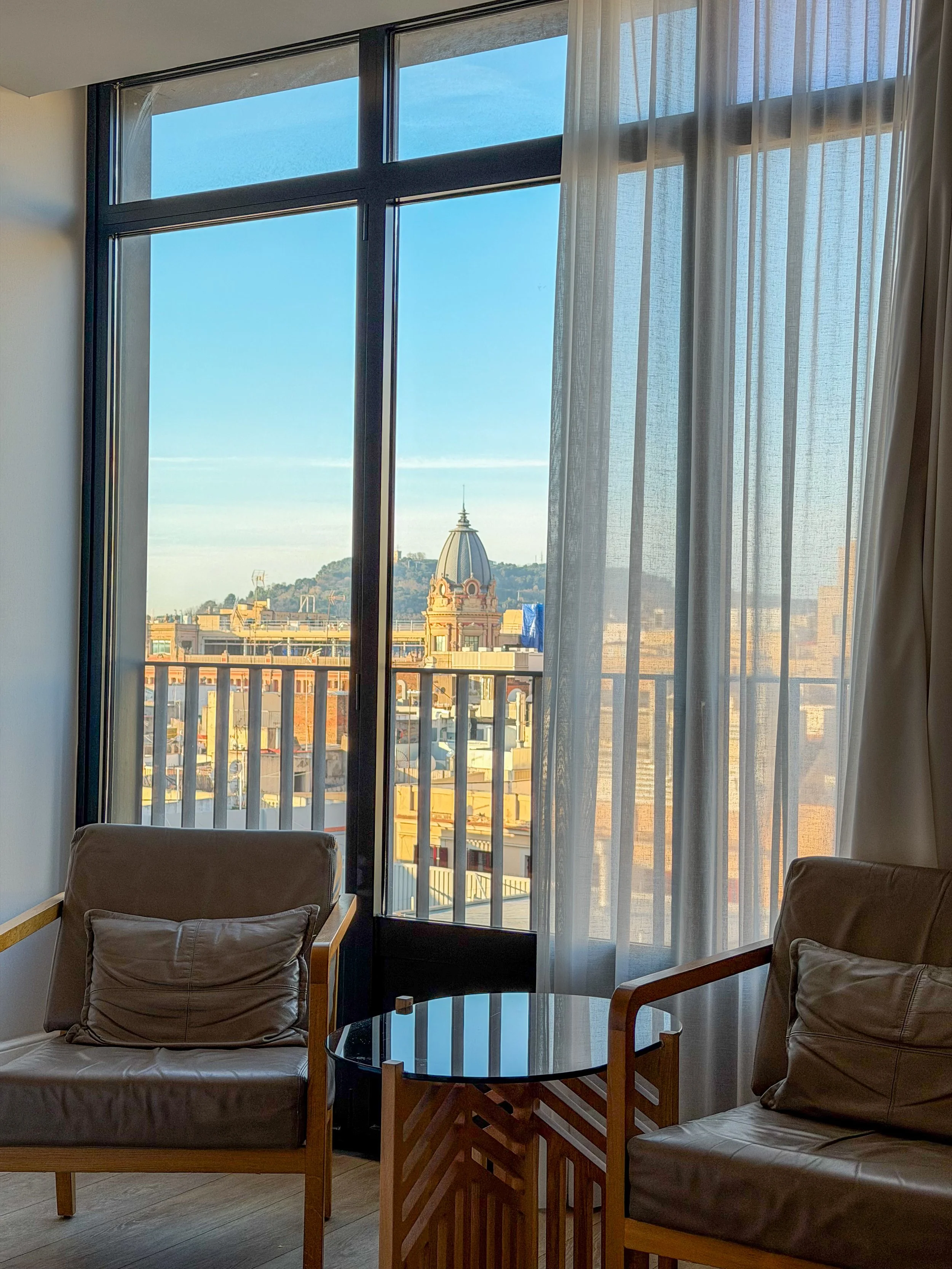 Guest room seating area with floor-to-ceiling windows and views over Barcelona’s rooftops, H10 Cubik Barcelona – Barcelona, Spain