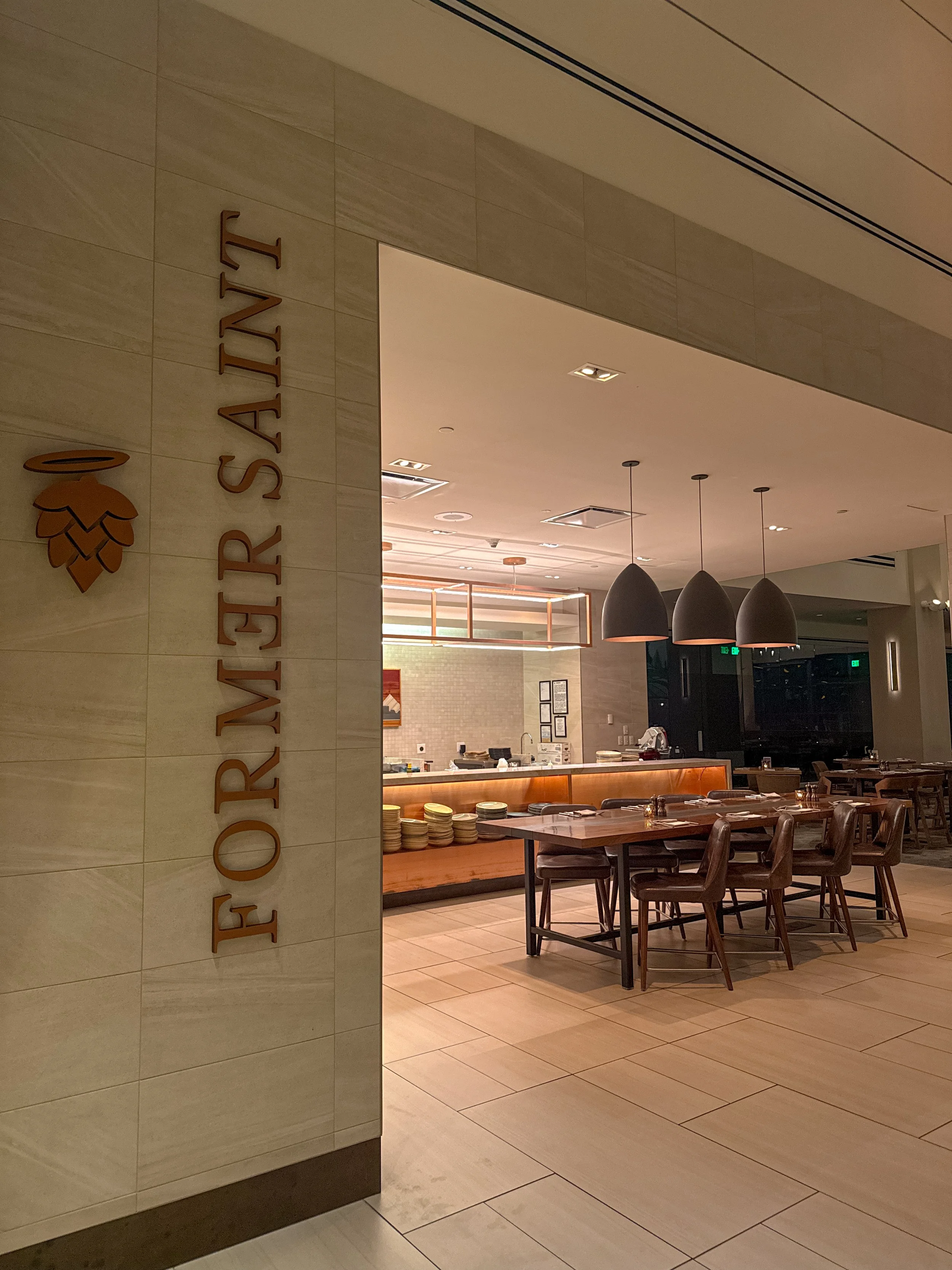 Entrance to Former Saint restaurant featuring contemporary dining tables, pendant lighting, and an open kitchen