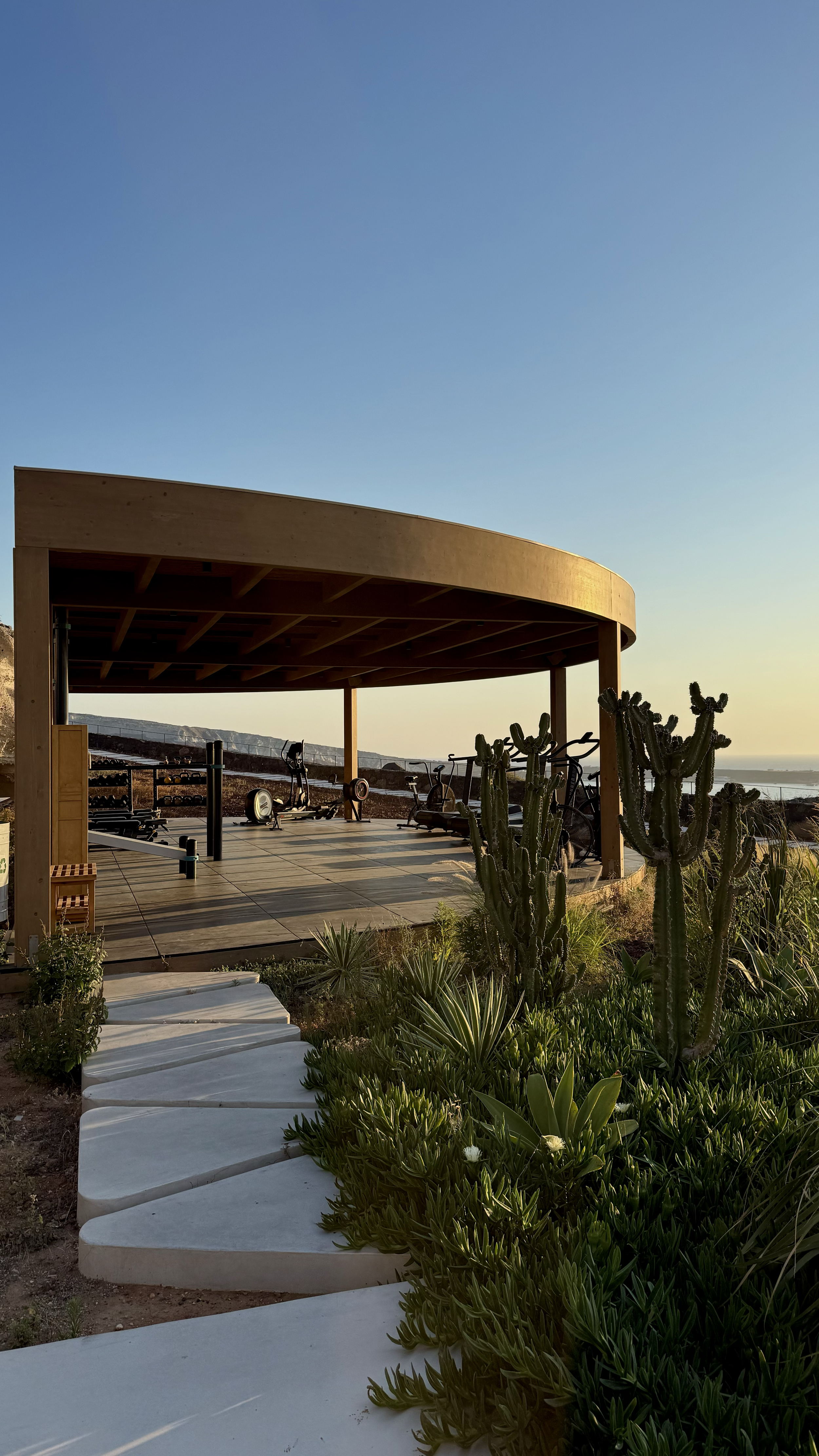 Open-air fitness pavilion with premium equipment overlooking Santorini’s volcanic coastline and the Aegean Sea