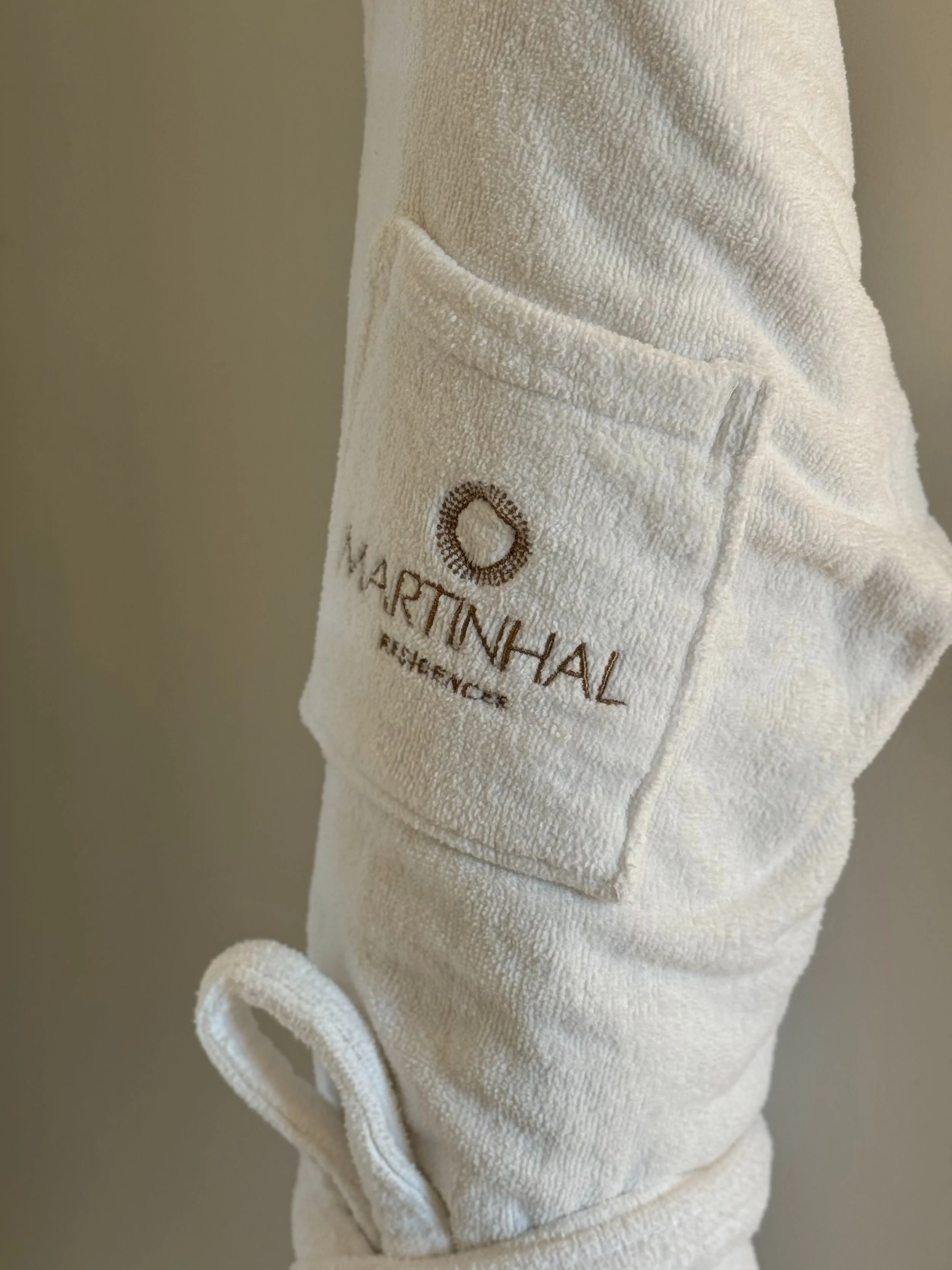 Plush white bathrobe embroidered with Martinhal branding, highlighting comfort, luxury amenities, and refined hospitality, Martinhal Lisbon Oriente – Lisbon, Portugal.