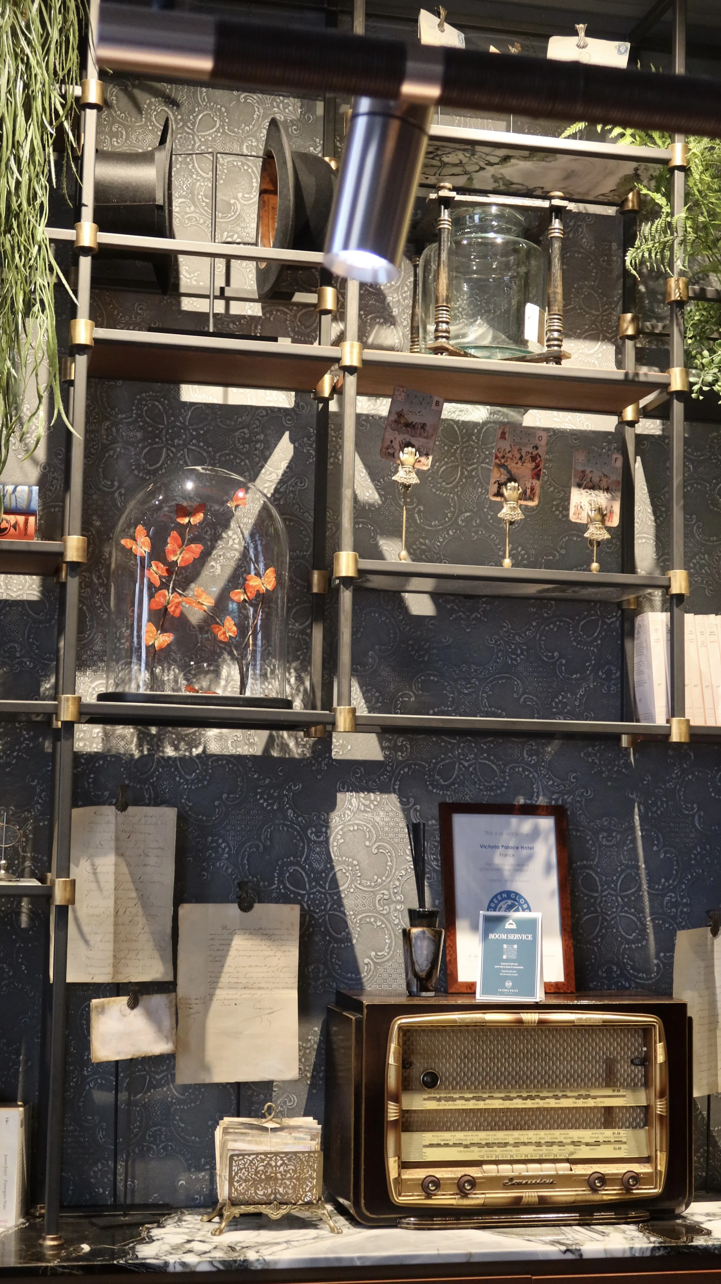 Decorative shelving with antique radio, framed certificates, glass dome display, and curated heritage details, Victoria Palace Hotel – Paris, France.