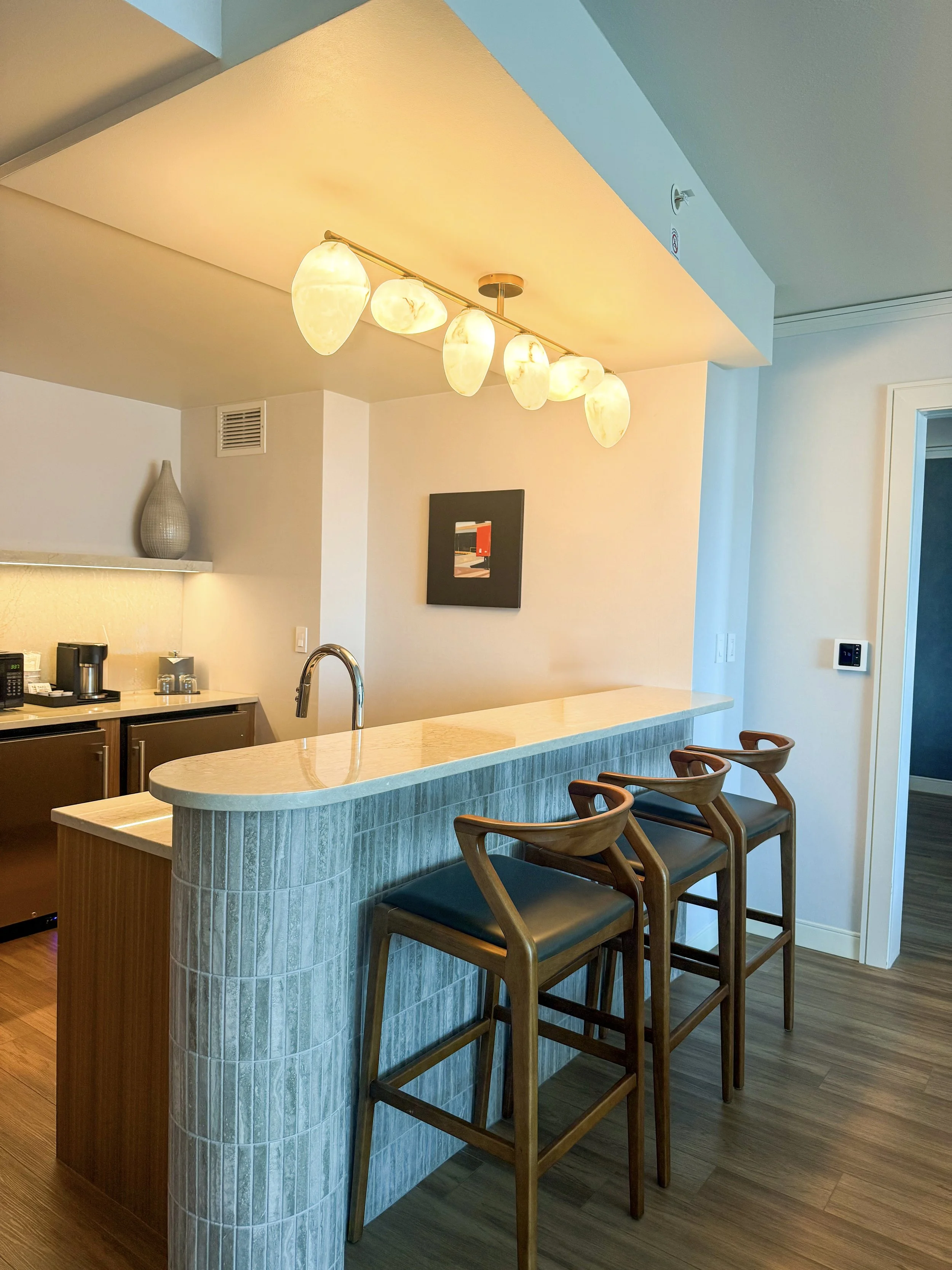 Contemporary suite kitchen featuring a marble breakfast counter, wooden bar stools, and pendant lighting