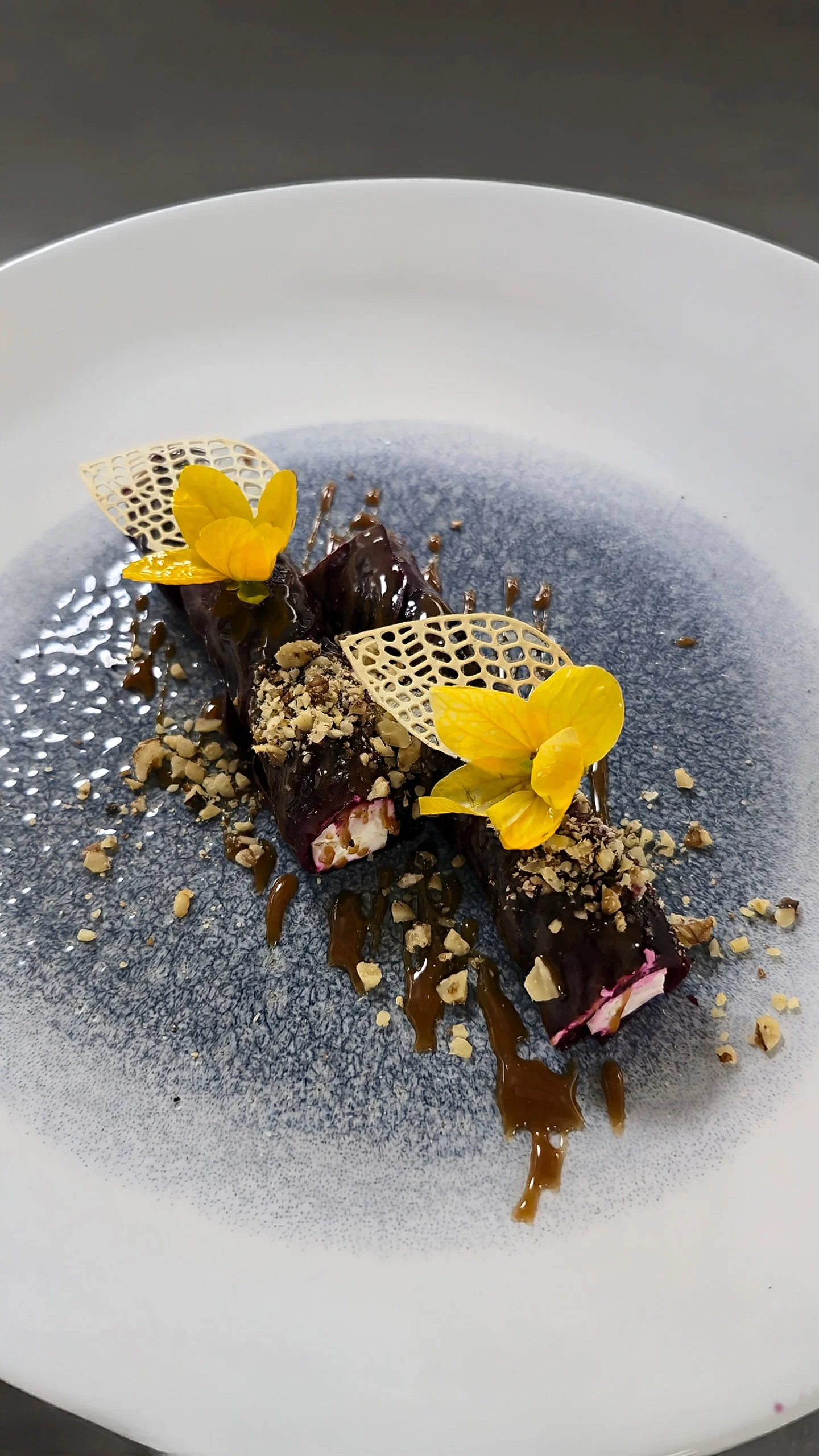 Artistic dessert plated with chocolate glaze, caramel drizzle, crushed nuts, and edible yellow flowers, Kempinski Hotel Aqaba Red Sea – Aqaba, Jordan.