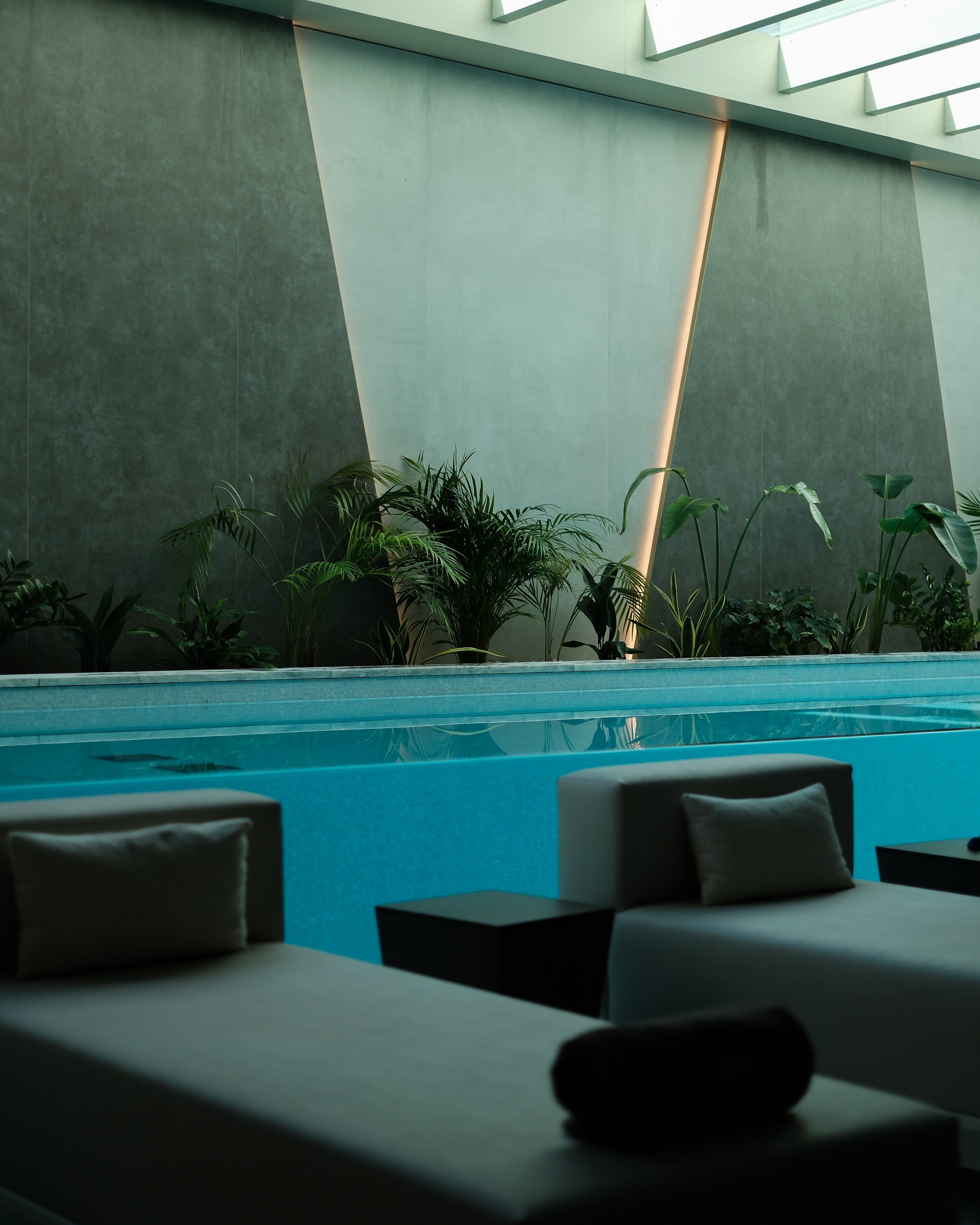 Softly lit indoor pool framed by geometric wall lighting, lush greenery, and modern lounge beds — Hyatt Regency Lisbon