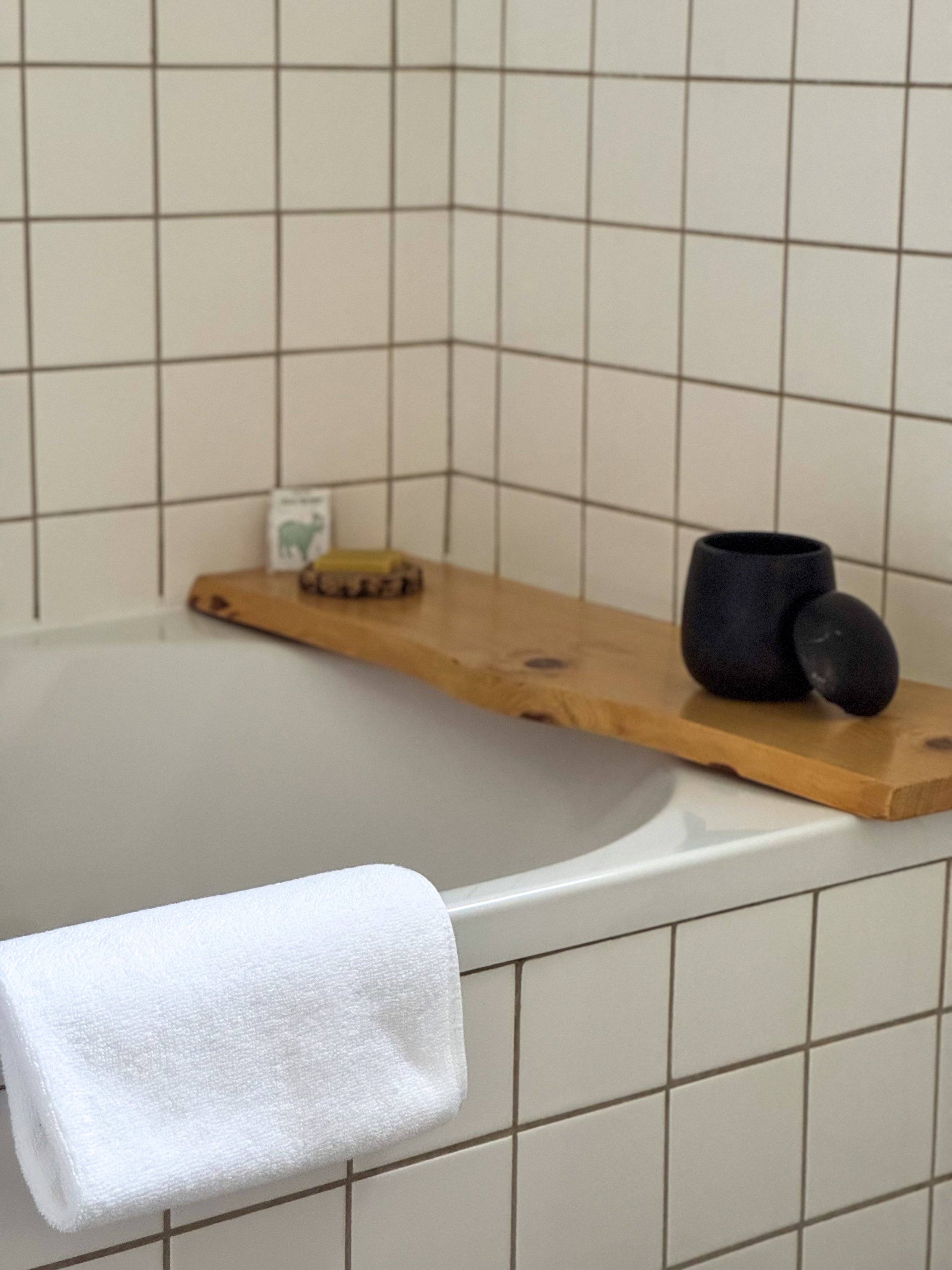 Minimalist bathroom with soaking bathtub and handcrafted wooden bath shelf at Chão do Rio