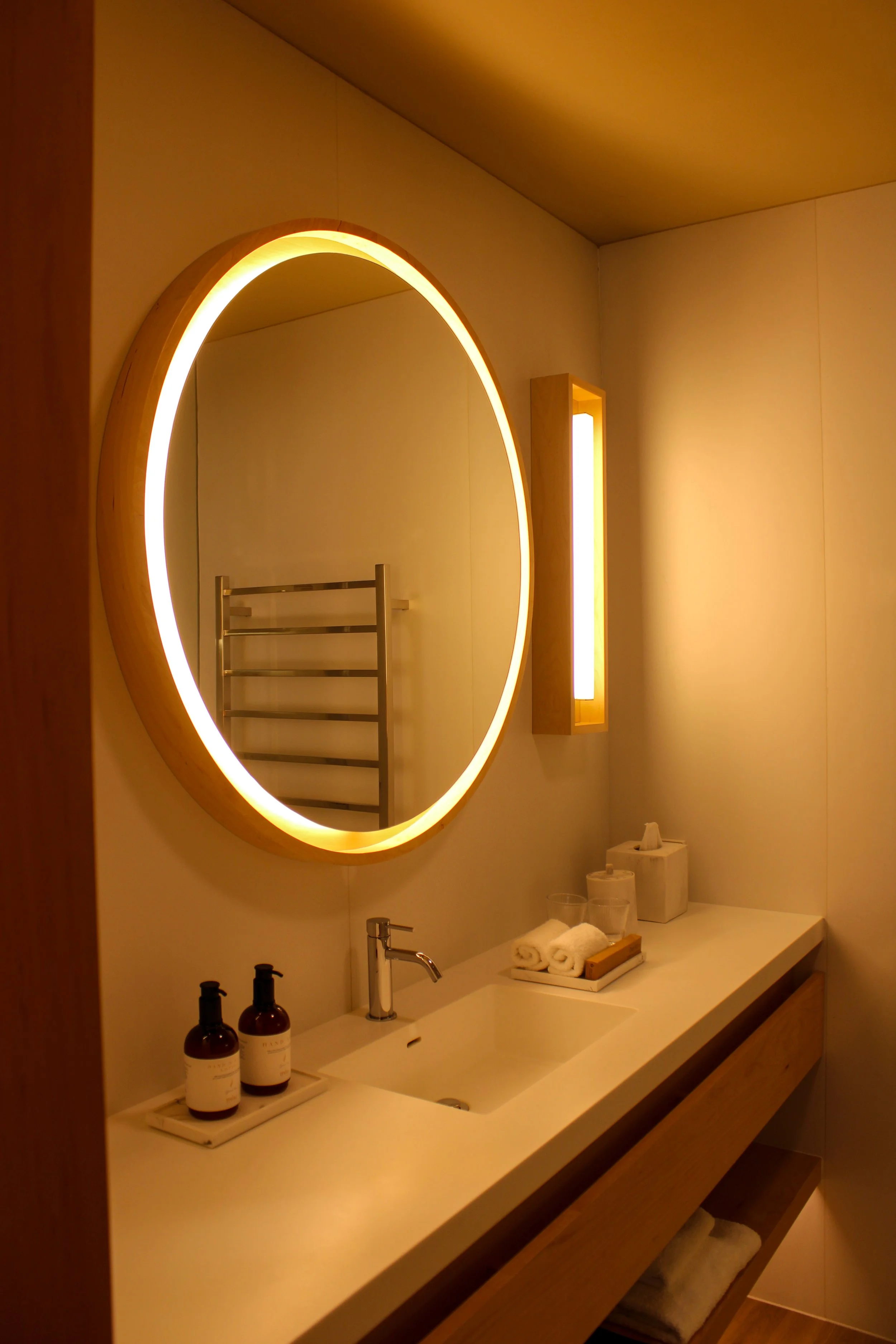 Minimalist bathroom featuring a circular illuminated mirror and modern finishes