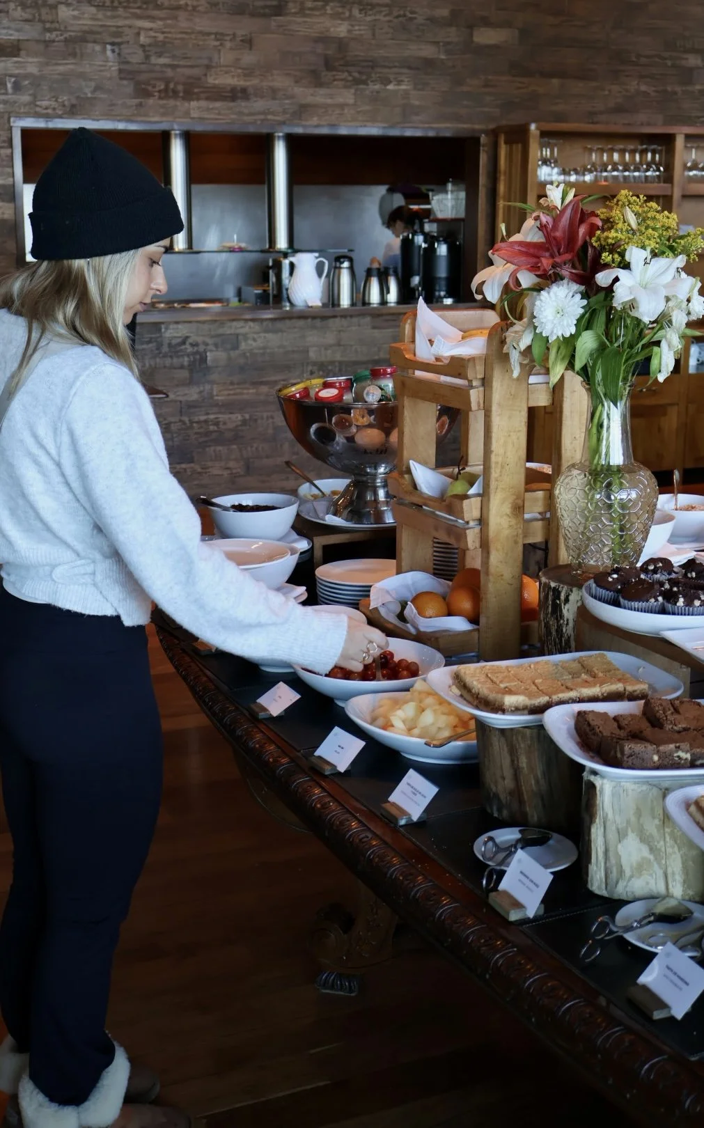 Guest exploring a generous breakfast buffet with fresh fruit, pastries, flowers, and rustic wooden displays