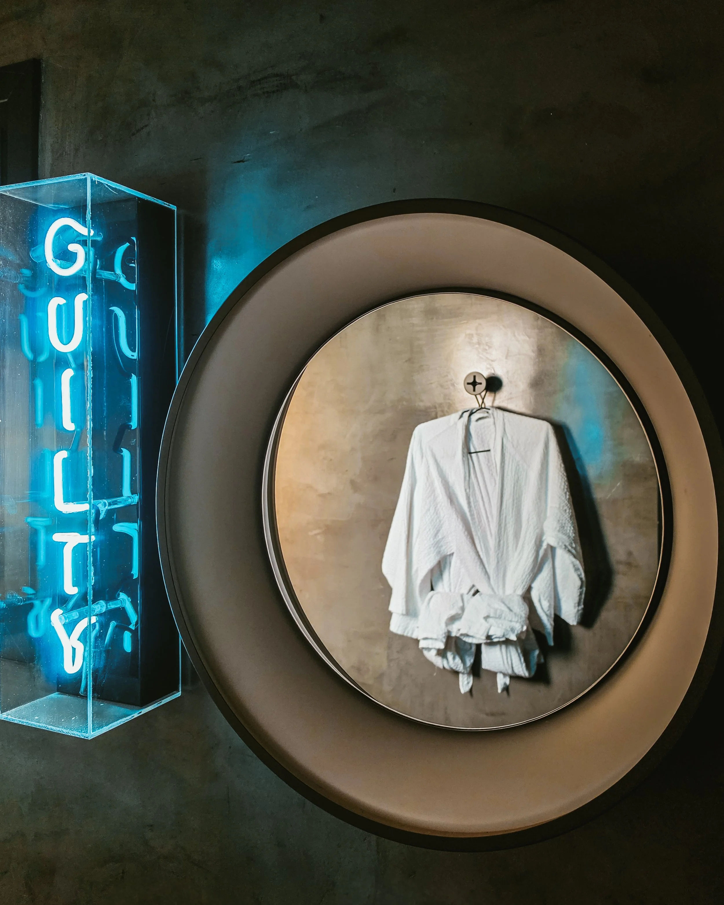 Luxury bathrobes reflected in a modern circular mirror beside artistic neon lighting and stylish décor