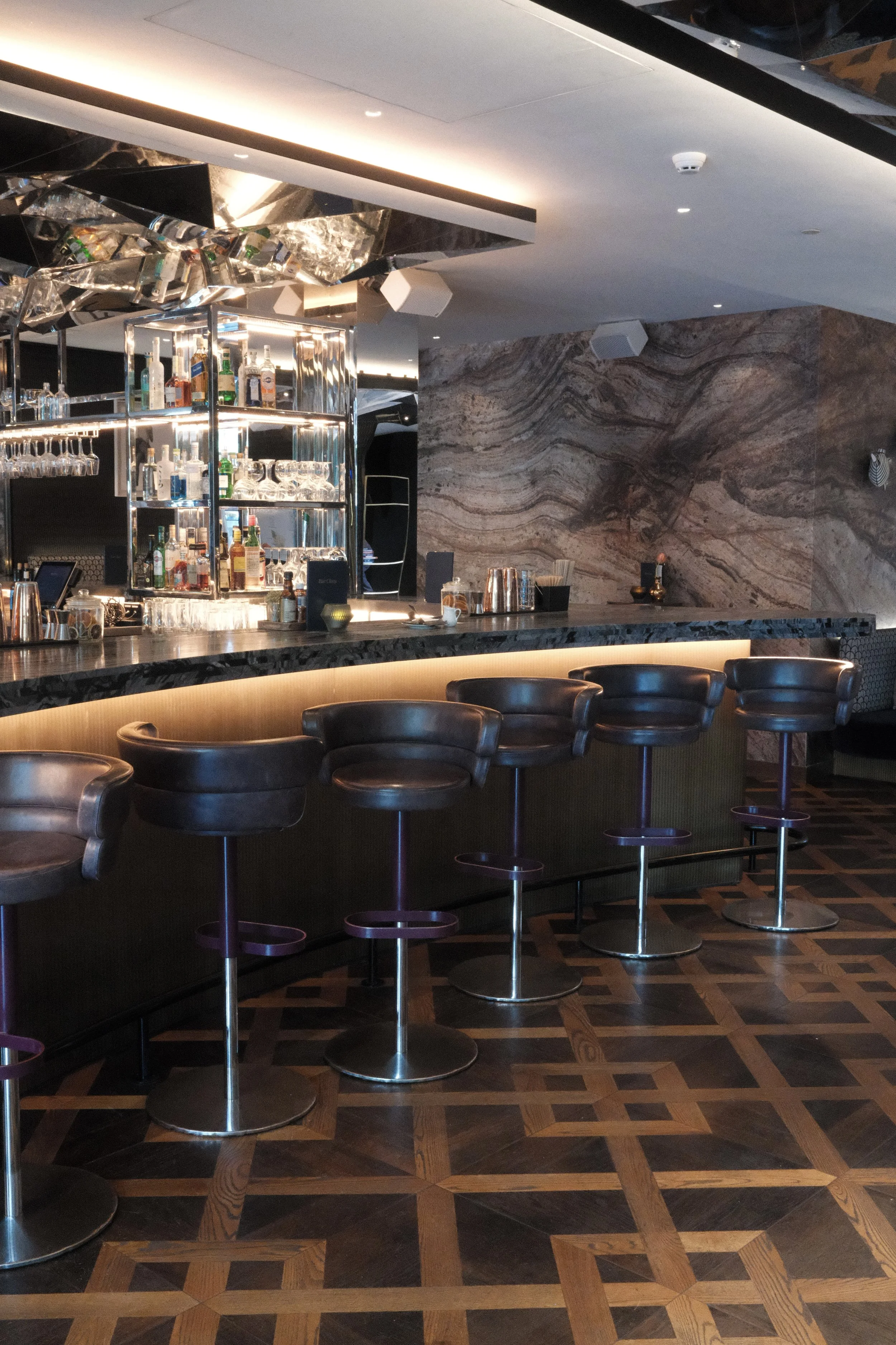 Elegant marble cocktail bar with mirrored ceiling and refined seating at Bar Claes