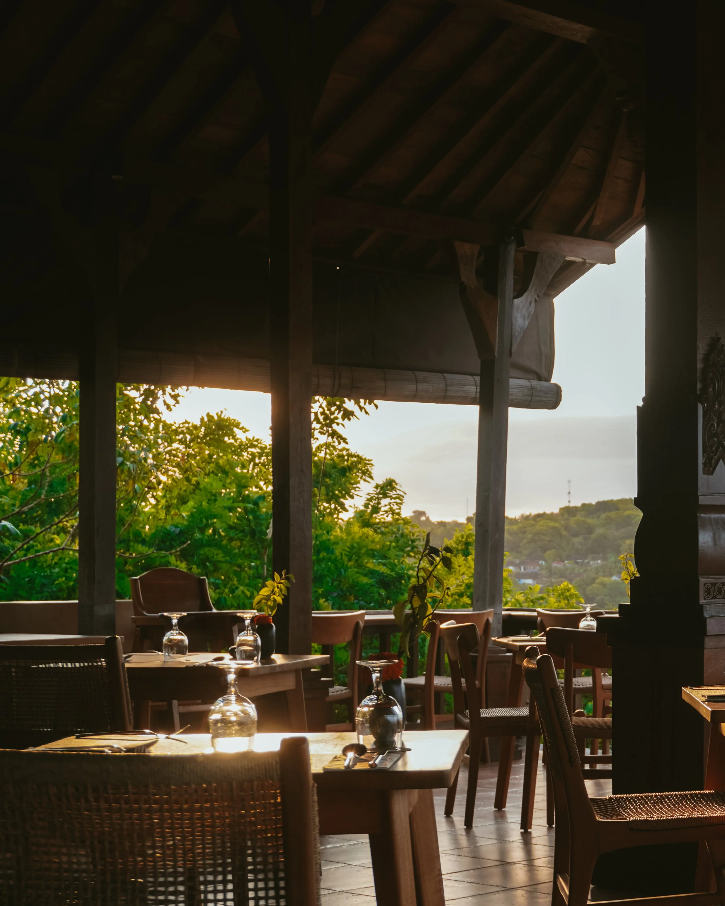 Open-air restaurant terrace with wooden tables and sunset jungle views at Pramana Nusa Ceningan Resort Bali