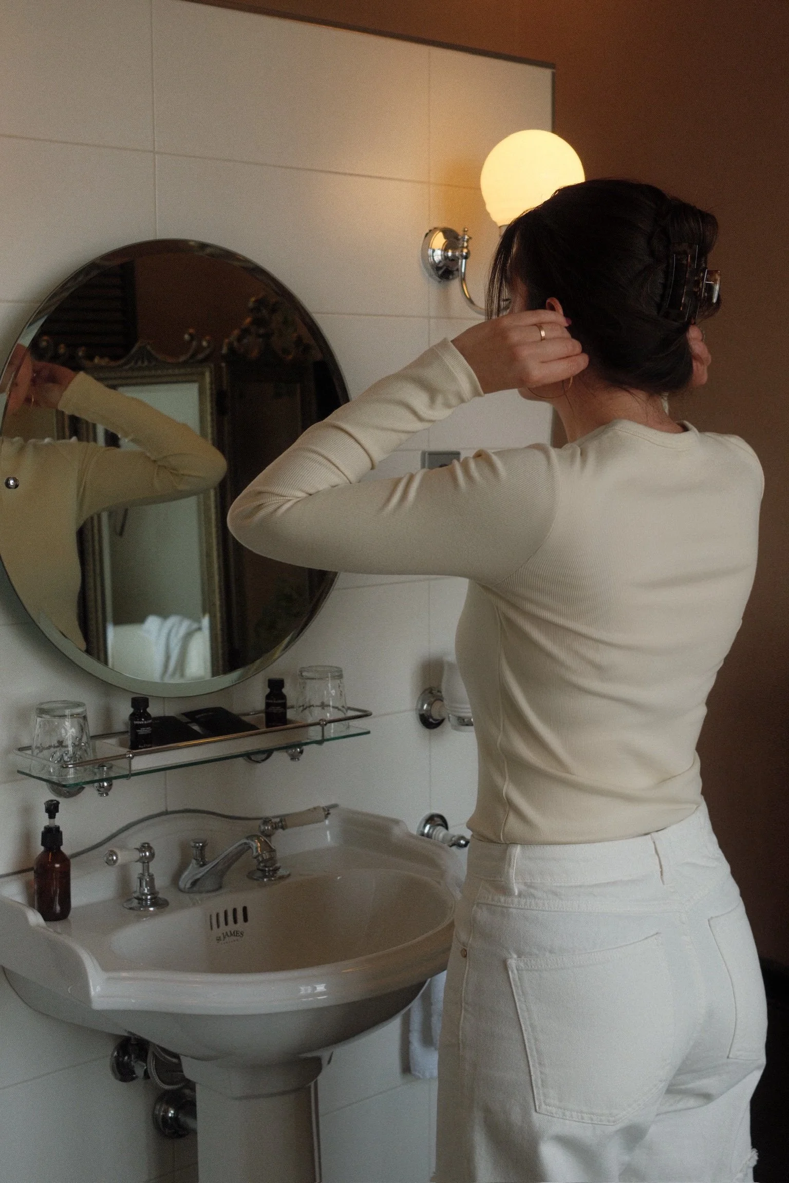 Guest preparing in bathroom mirror with classic sink and warm lighting at Suite Hotel Pincoffs Rotterdam