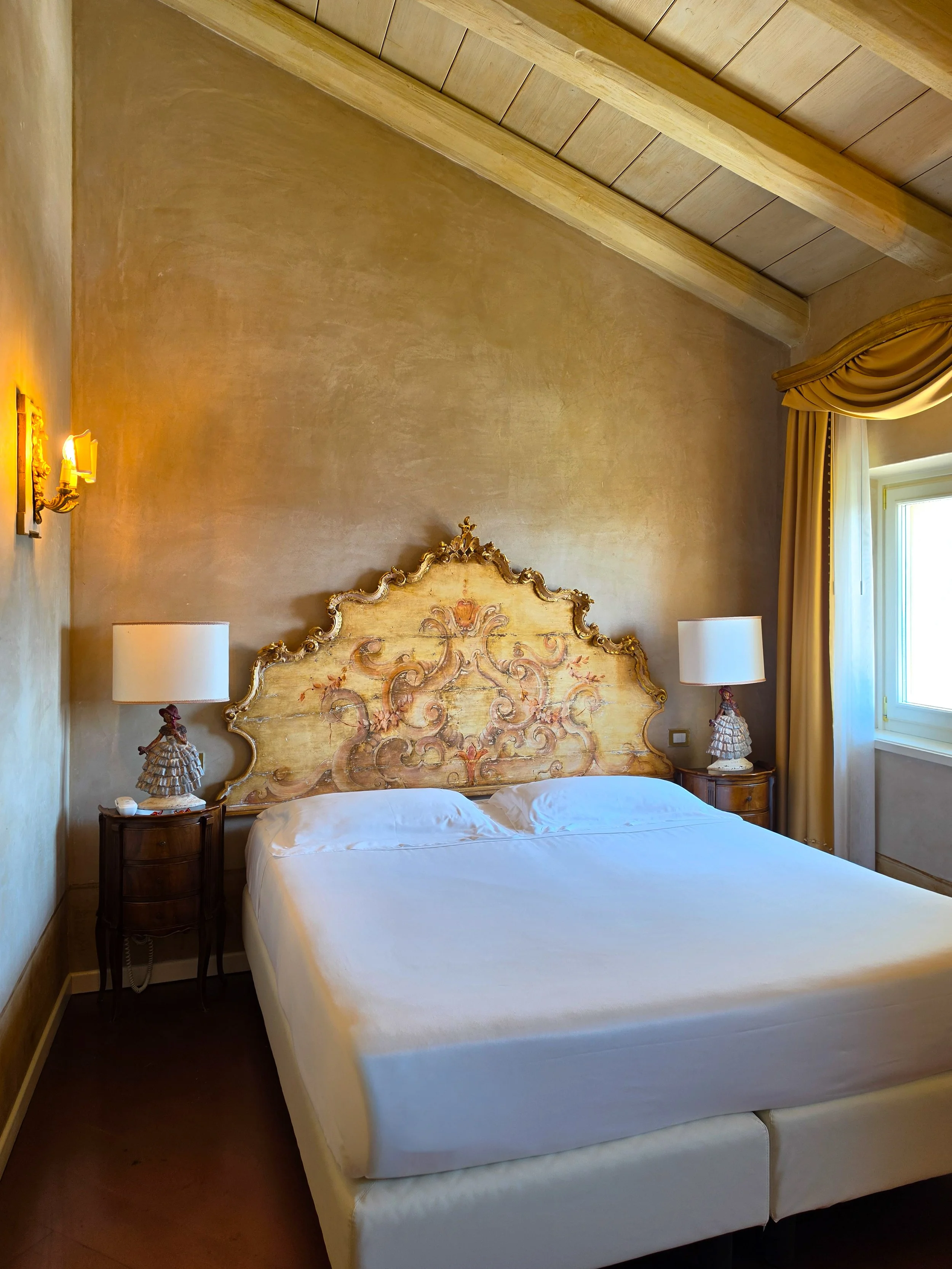 Elegant guest room featuring a handcrafted decorative headboard, wooden beams, and timeless Italian design