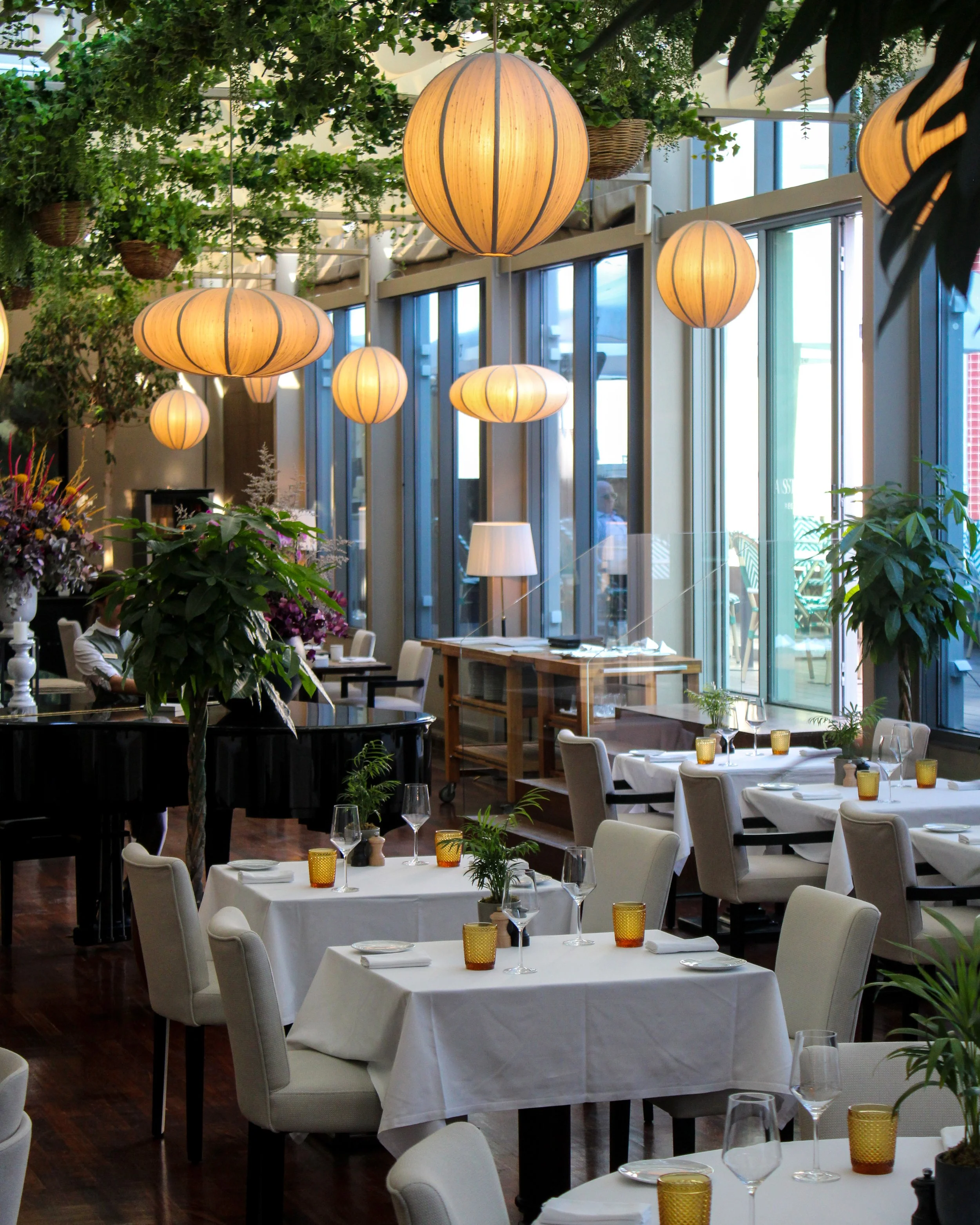 Bright restaurant with lush greenery, contemporary lighting, and elegant tables