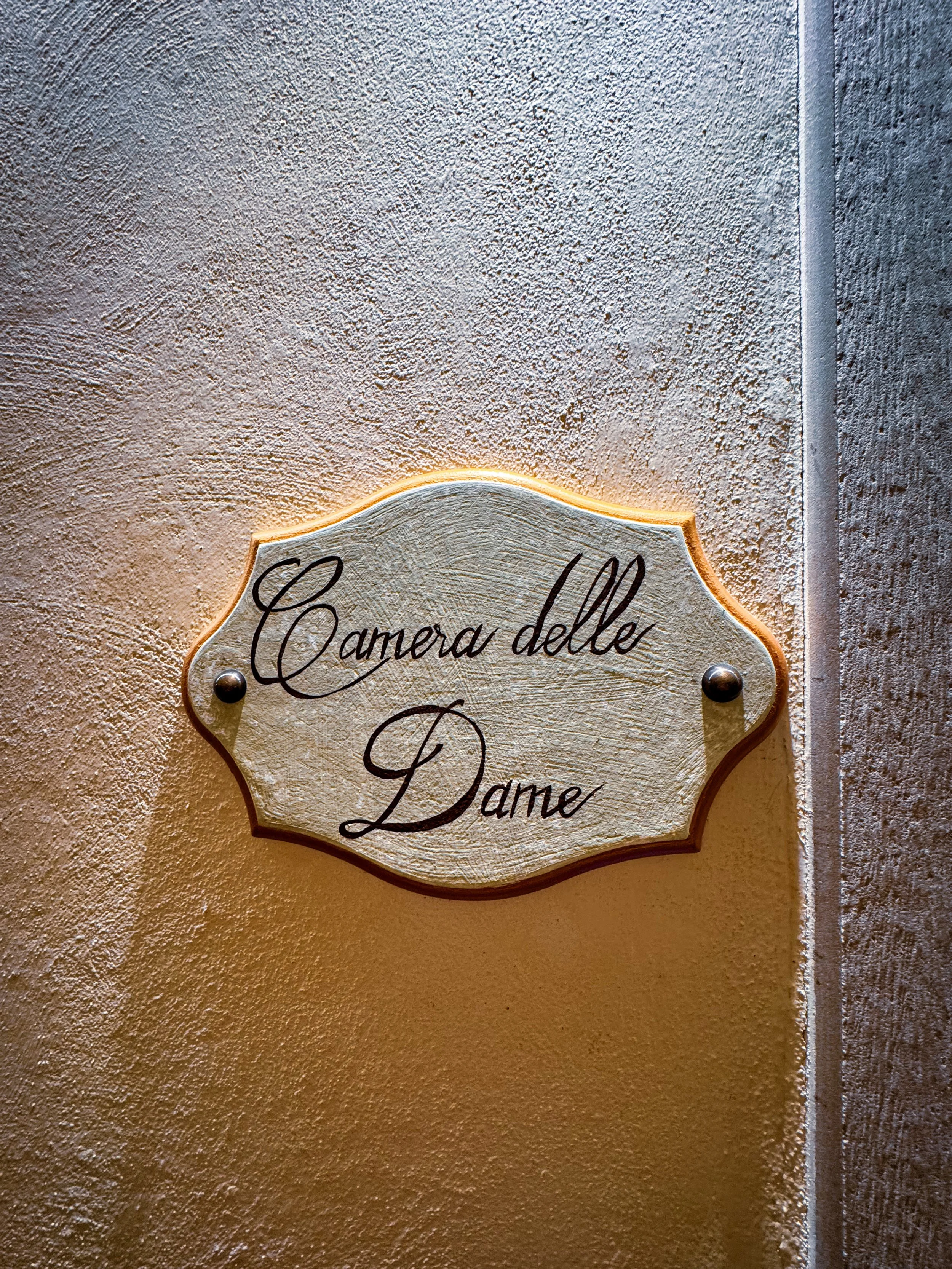 Vintage-style room plaque reading “Camera delle Dame” at historic property, Art Hotel Commercianti – Bologna, Italy.