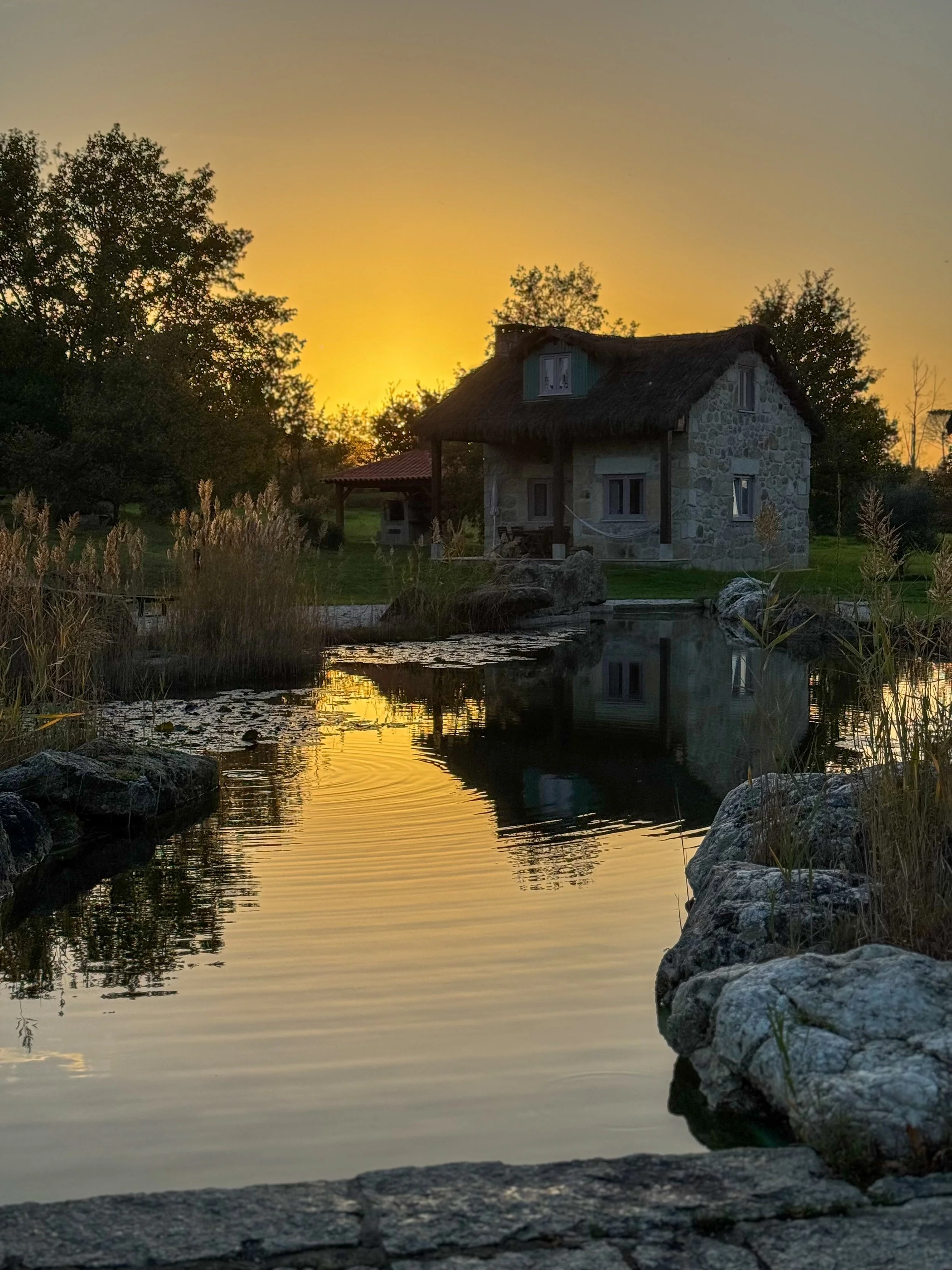Sunset over the natural swimming pond reflecting a traditional stone cottage at Chão do Rio