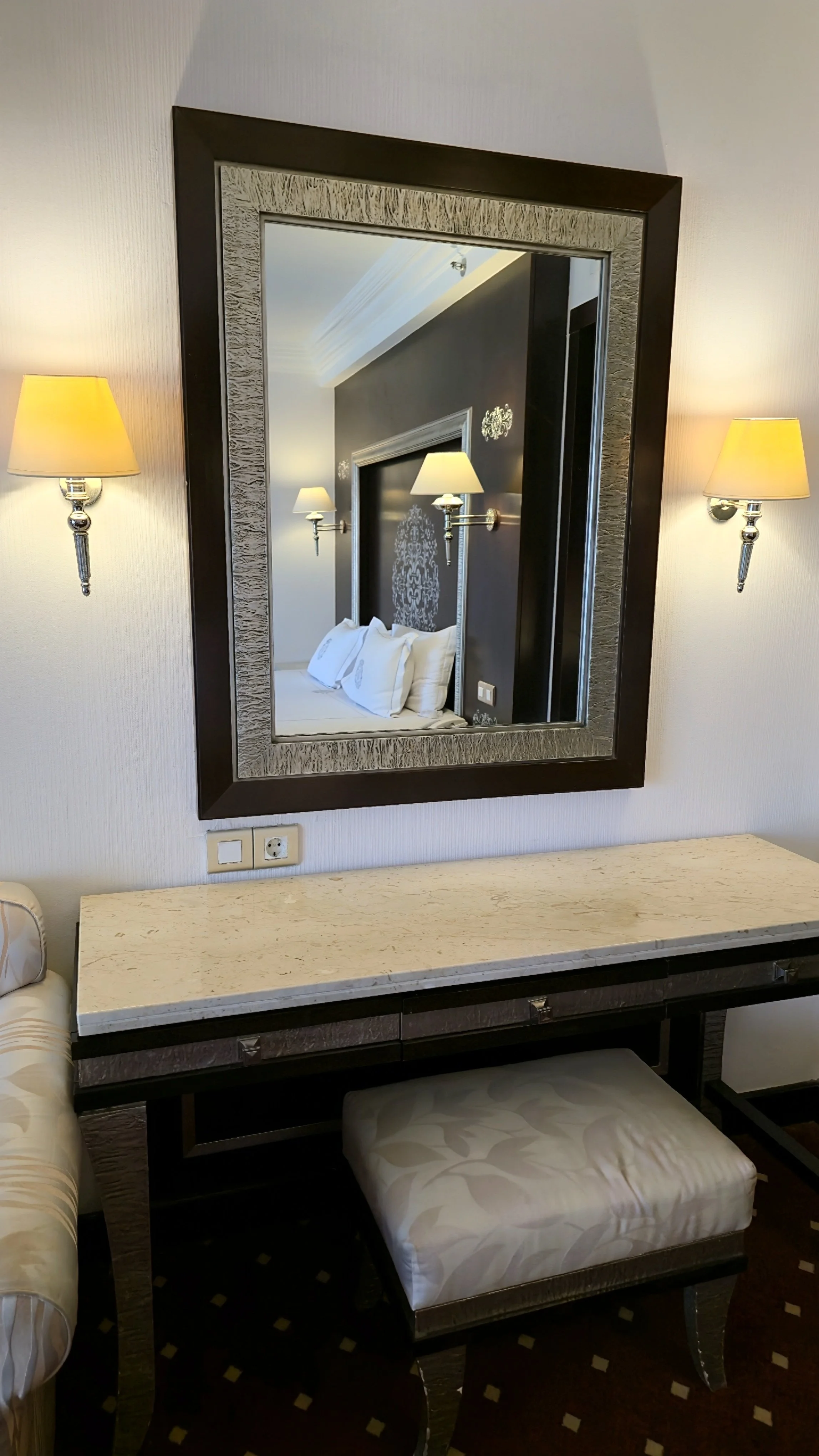 Framed mirror reflecting a refined bedroom with marble vanity and soft wall lighting details, Sonesta St. George Hotel Luxor.