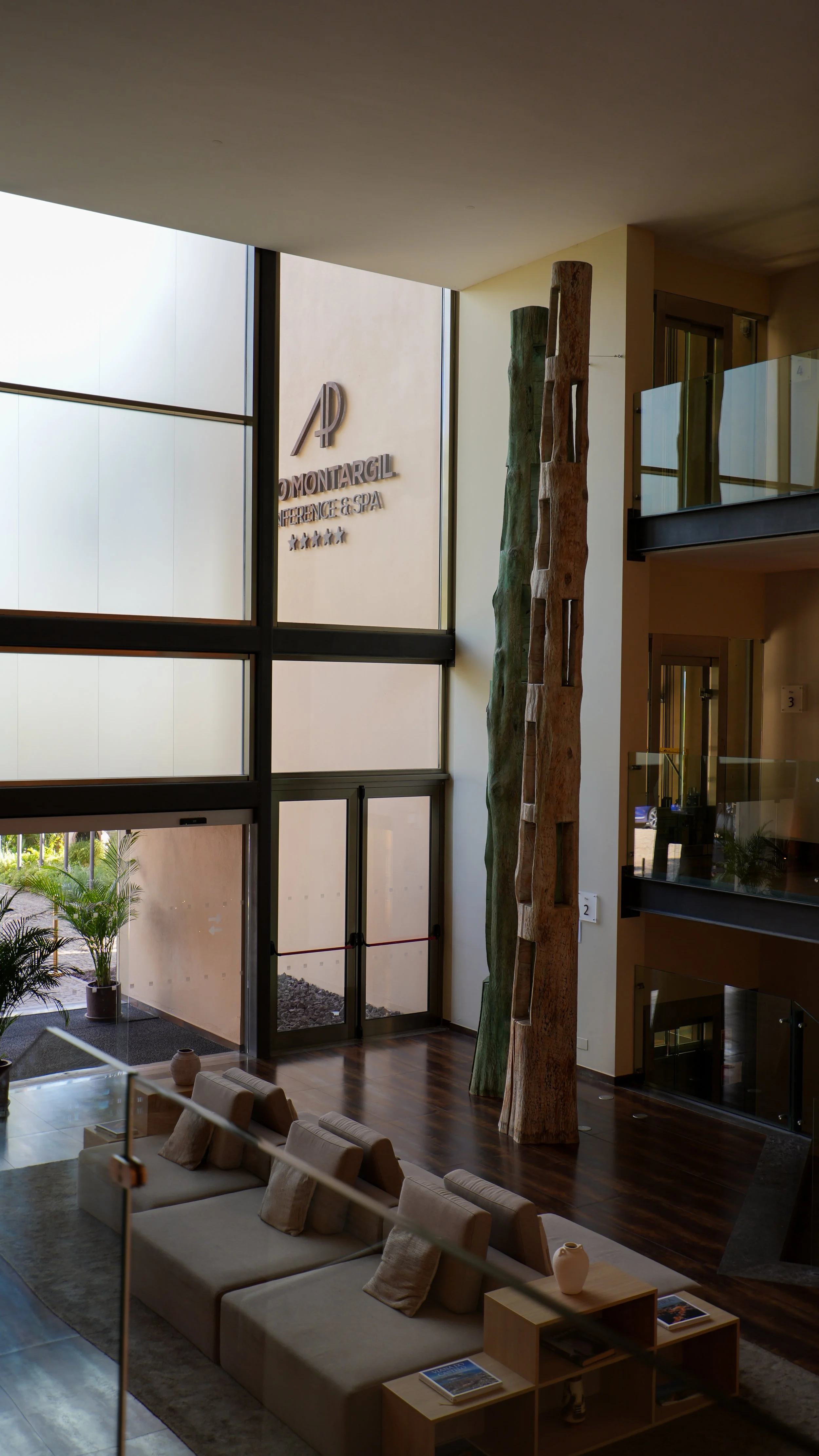 Spacious resort lobby featuring floor-to-ceiling windows, wooden sculptures, and comfortable lounge seating