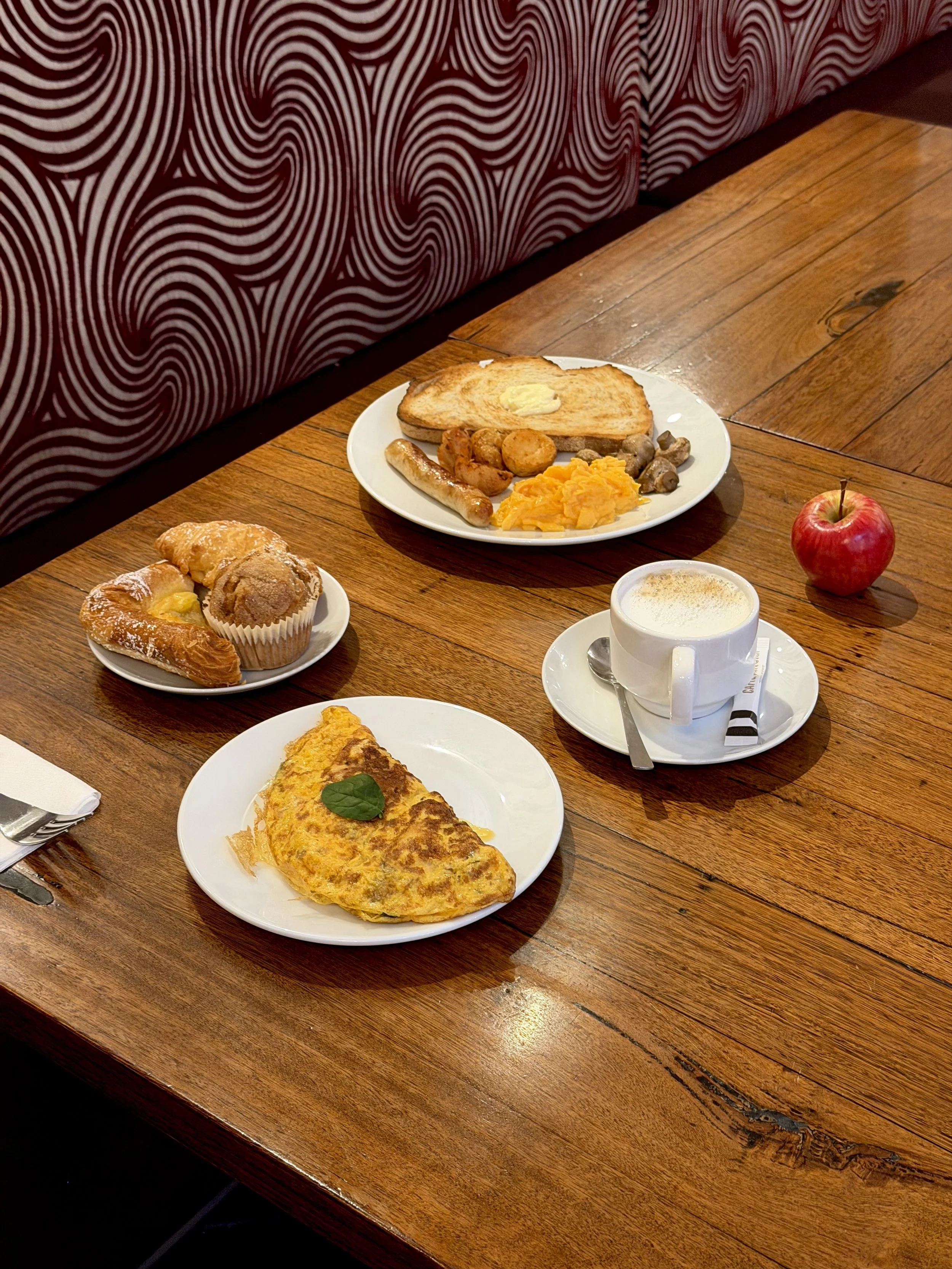 Hotel breakfast featuring scrambled eggs, sausages, toast, pastries, an omelette, and freshly prepared coffee