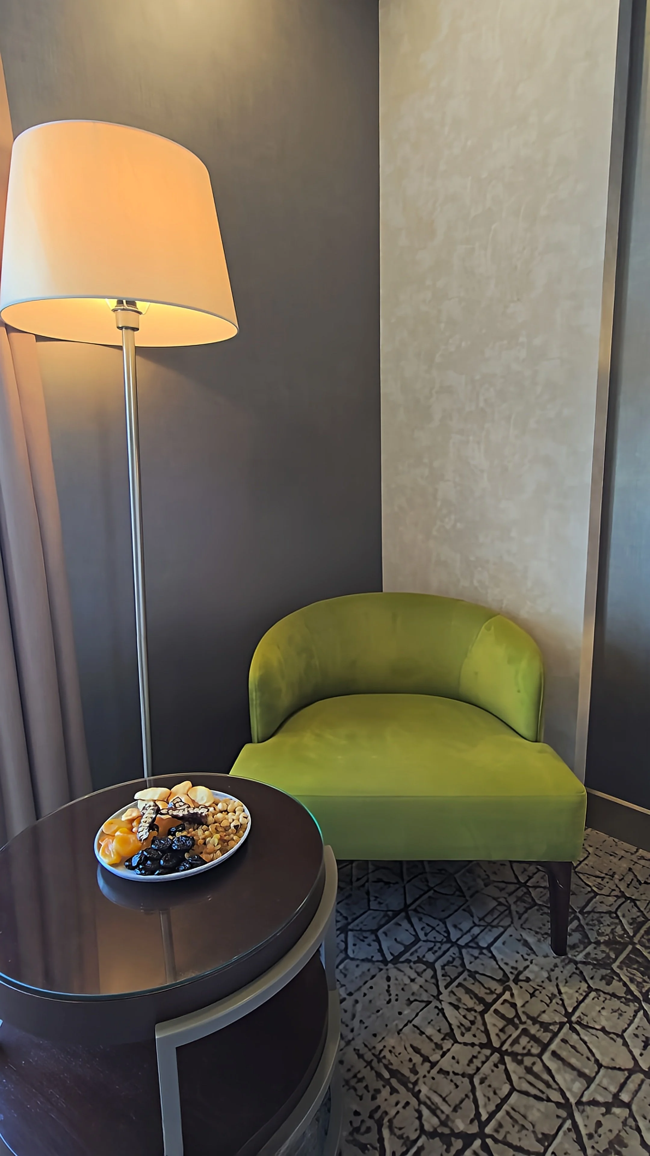 Elegant guest room seating area with a green velvet chair, floor lamp, and welcome treats