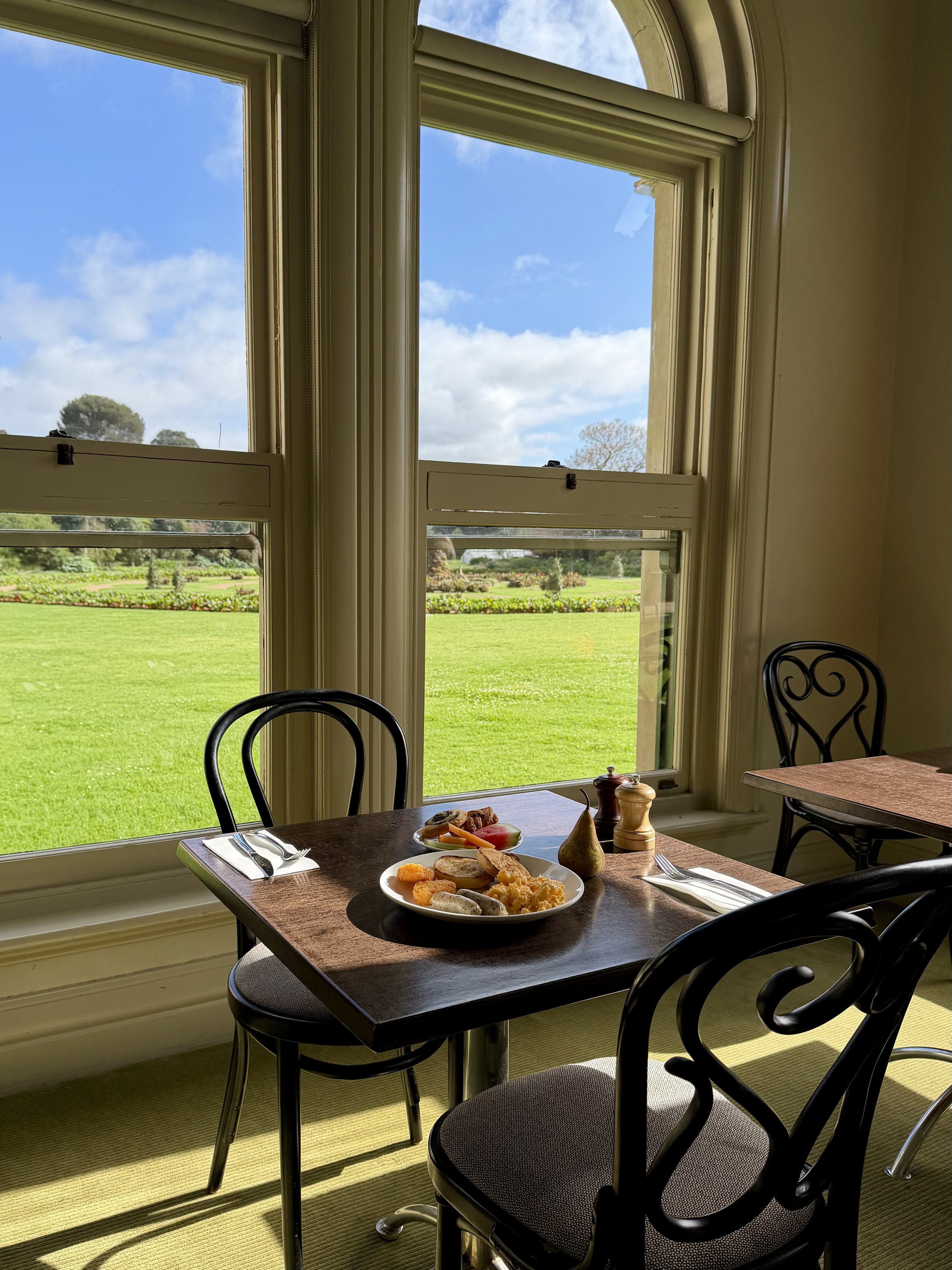 Breakfast table beside large arched windows overlooking beautifully maintained gardens and green lawns