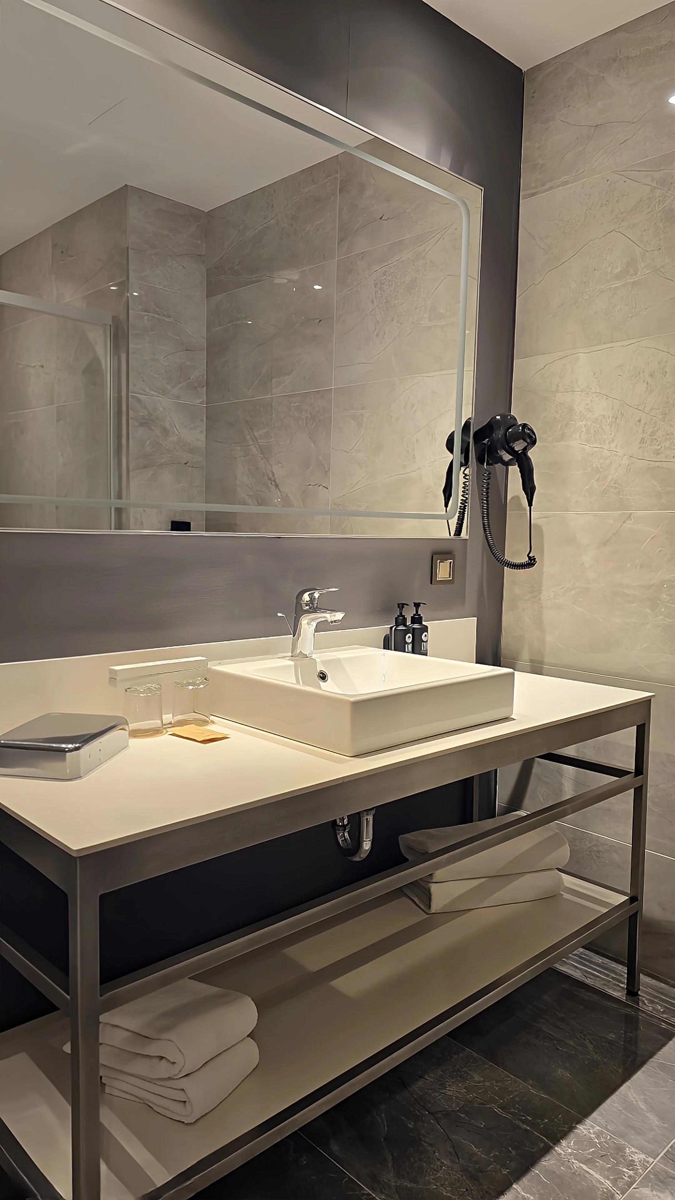 Modern marble bathroom with a spacious vanity, illuminated mirror, and walk-in shower
