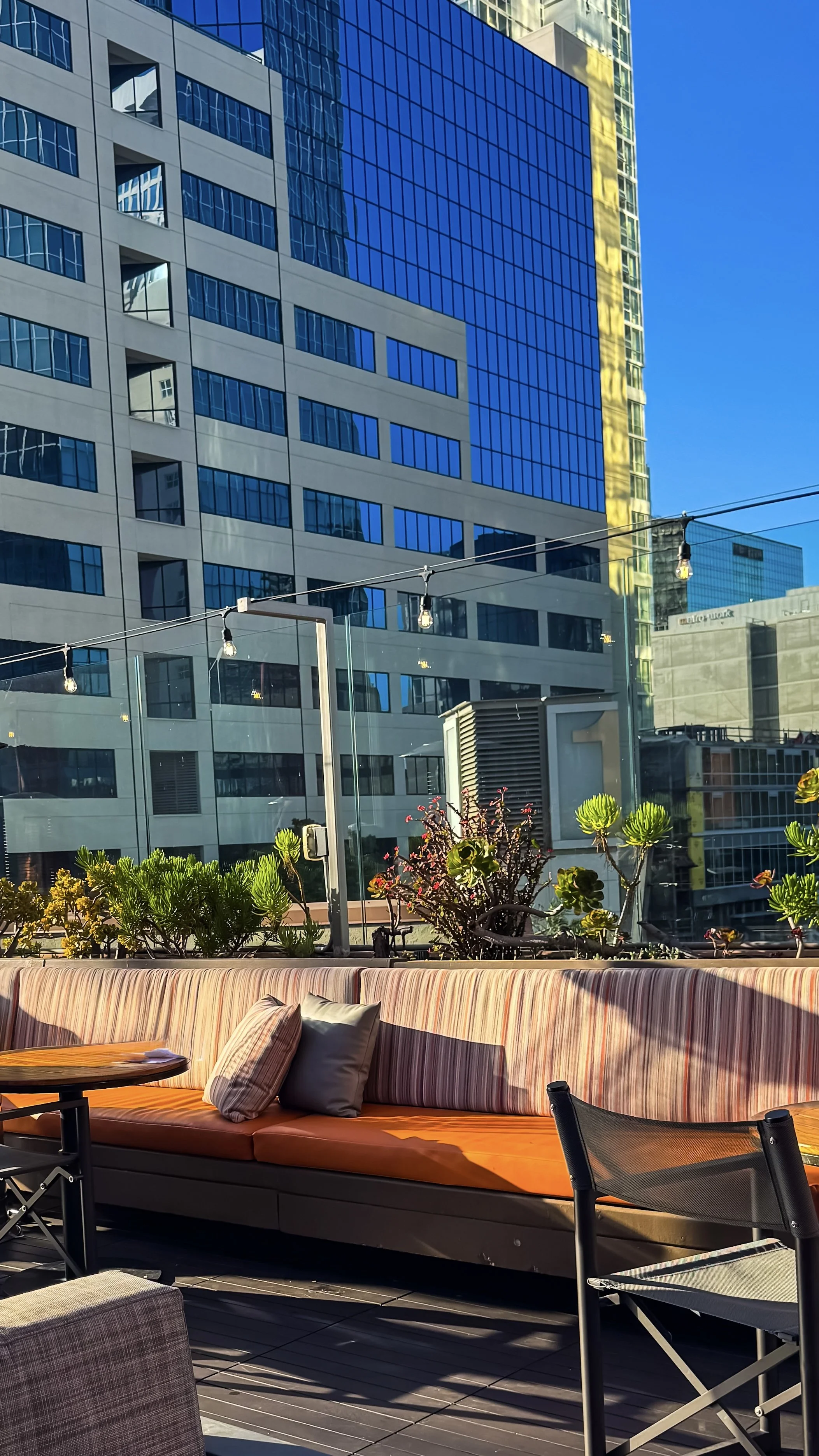 Rooftop lounge with orange cushioned seating, string lights, and city skyline views in warm afternoon light, Hotel Republic San Diego – San Diego, California.