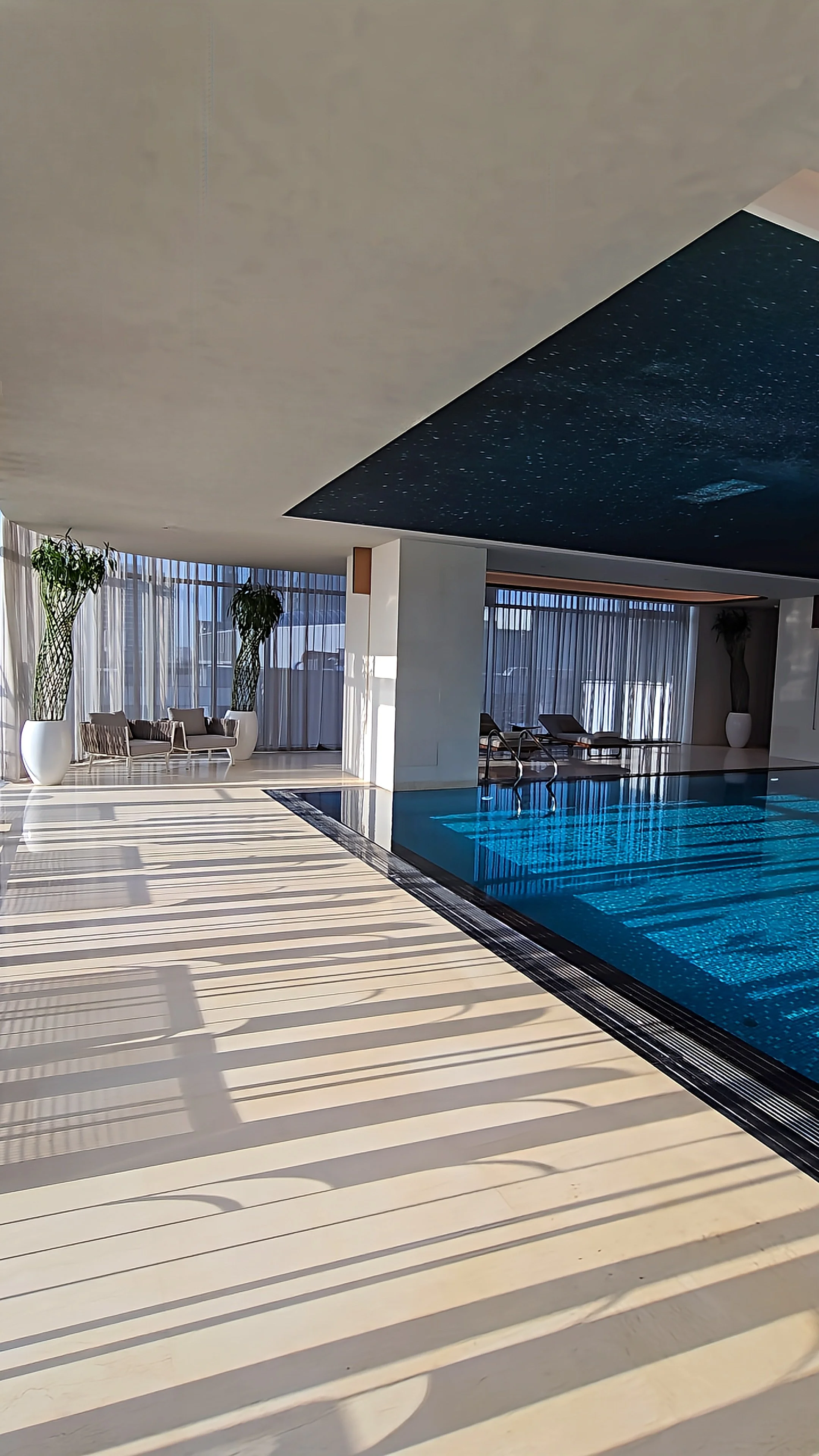 Modern indoor swimming pool with natural light, relaxation loungers, and tranquil wellness atmosphere