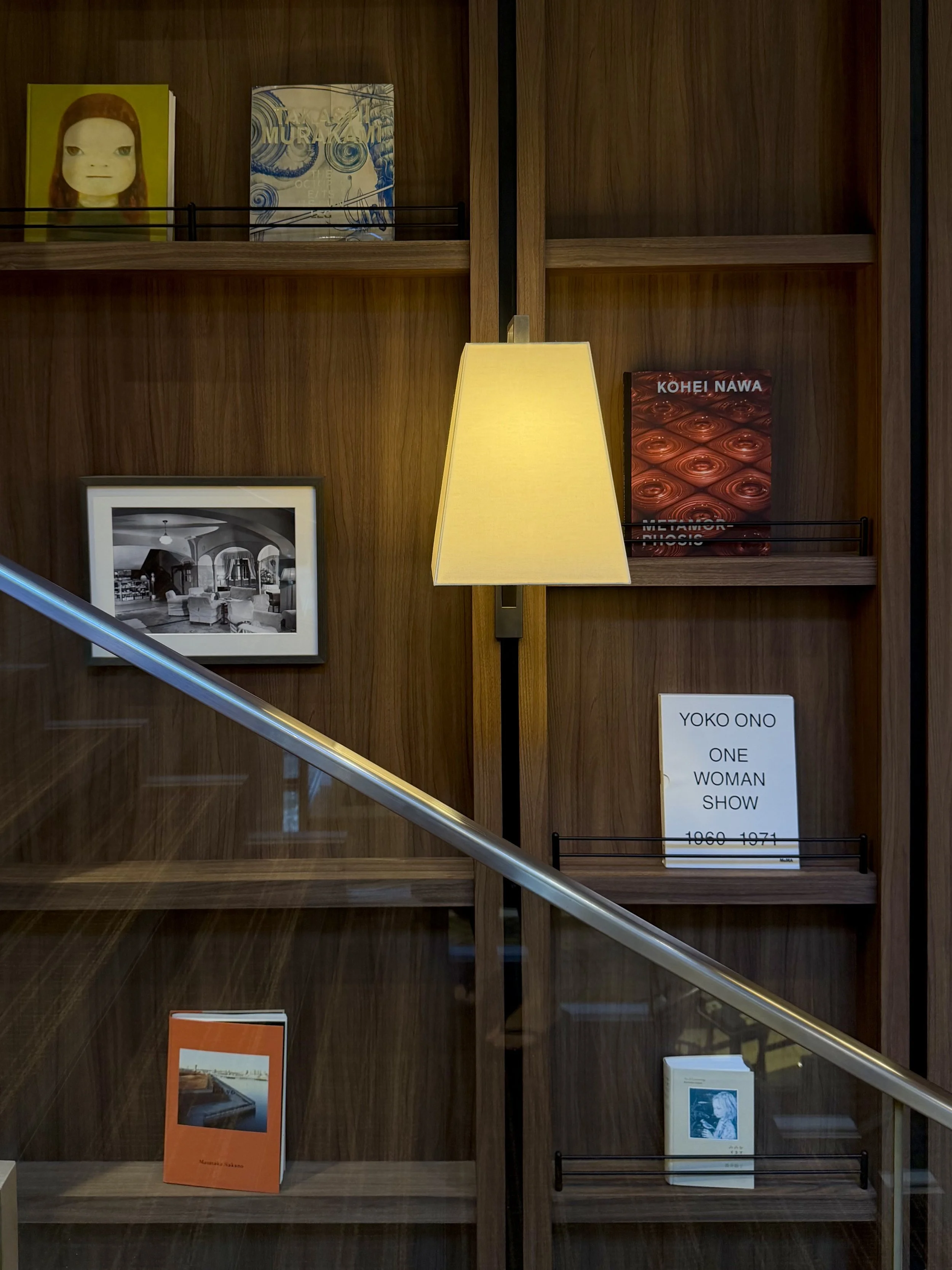 Curated art books displayed on wooden library shelves beside a softly illuminated wall lamp