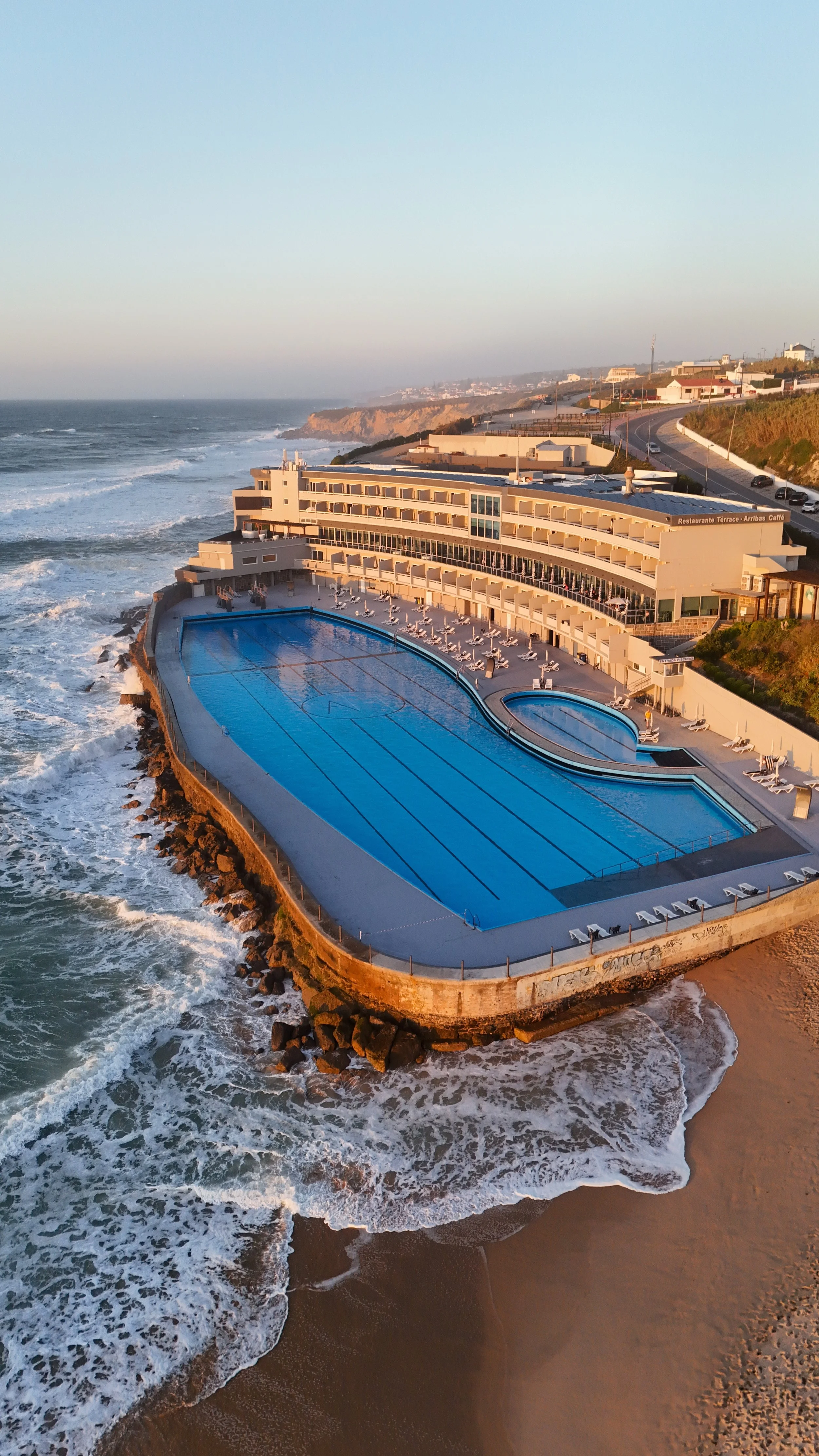 Aerial view of Arribas Hotel and its iconic oceanfront saltwater pool on the Sintra coastline at sunset