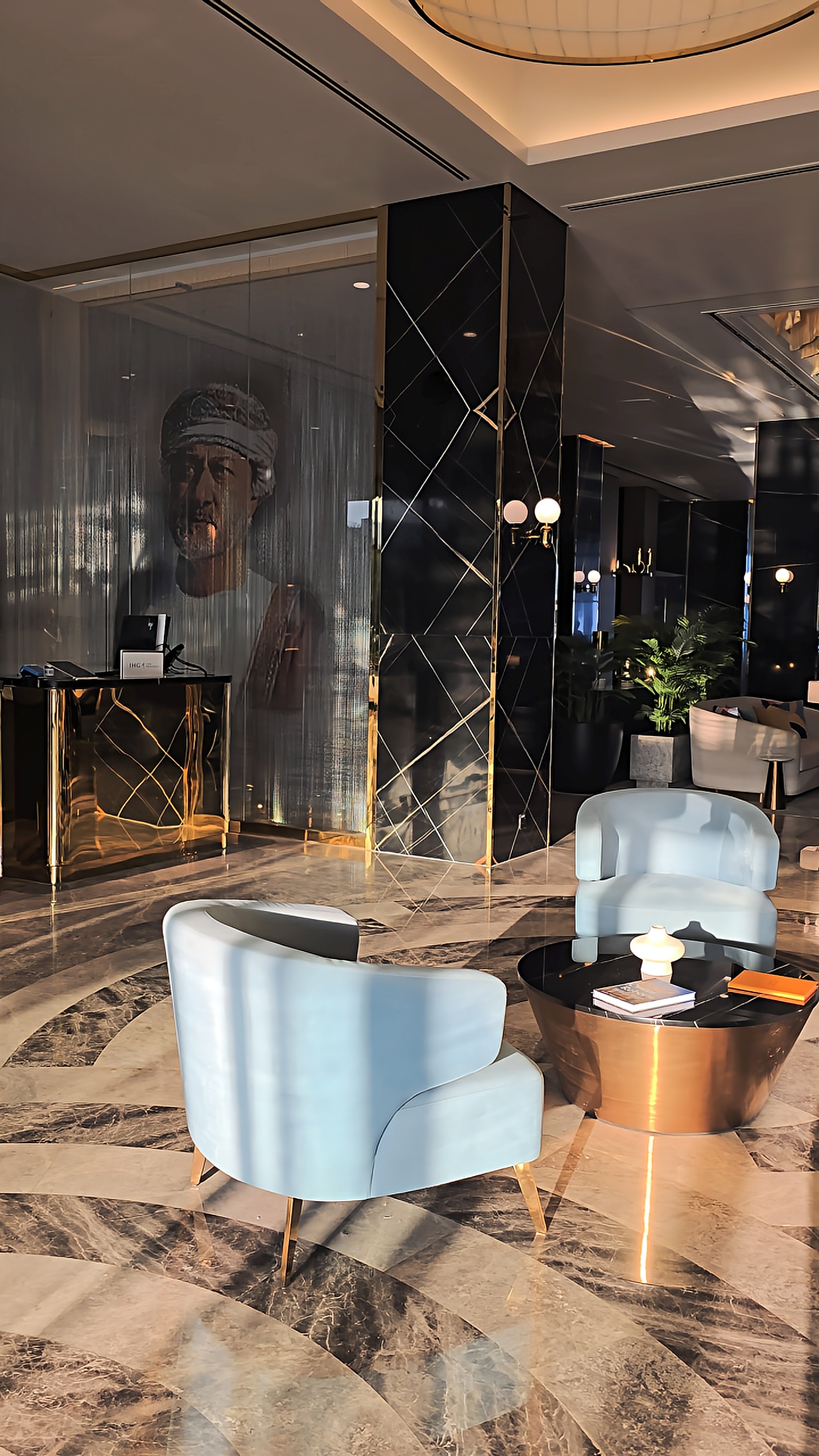 Elegant hotel lobby featuring marble floors, pale blue armchairs, black stone columns, and contemporary lighting