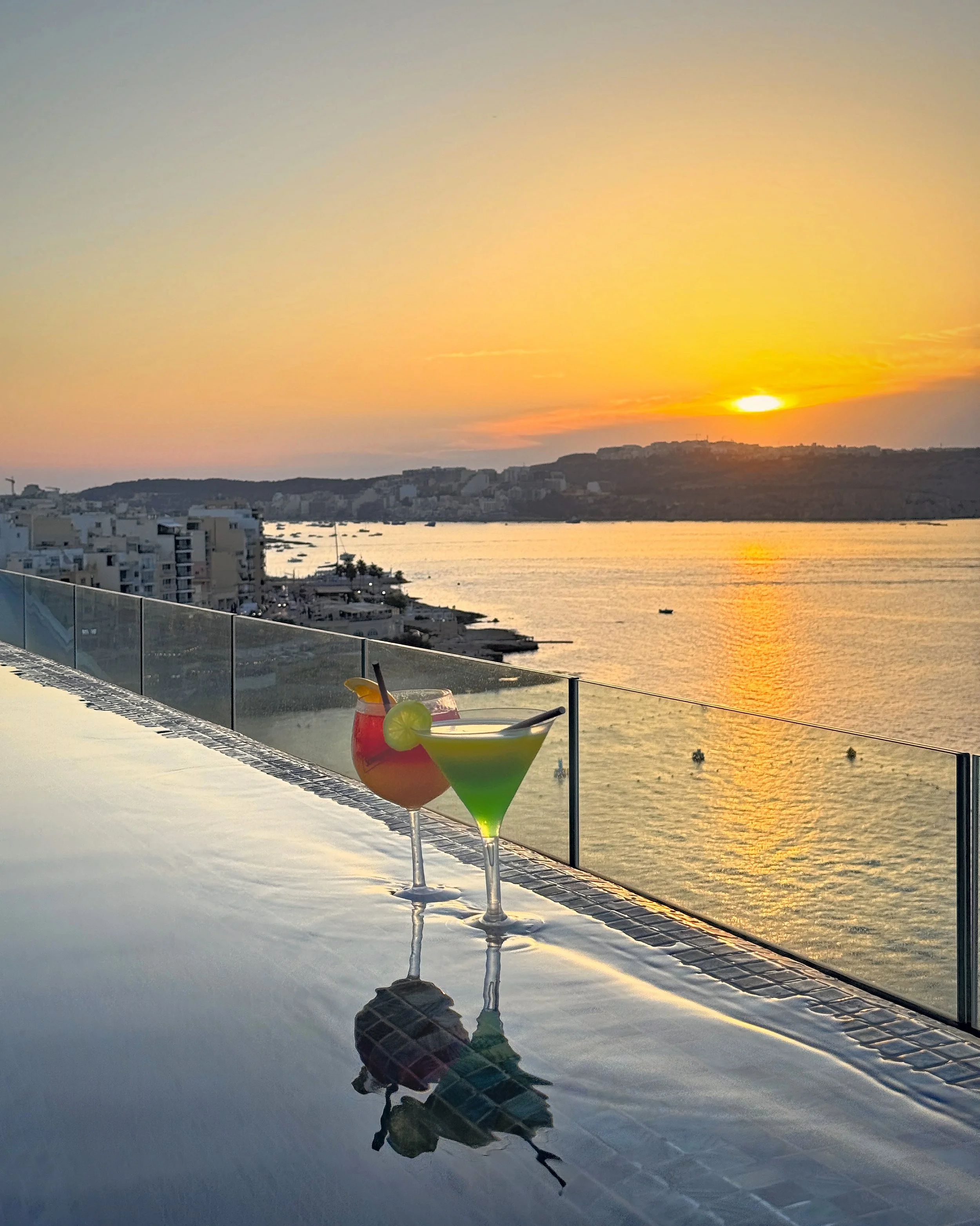 Colorful cocktails beside a rooftop pool overlooking the Mediterranean at sunset