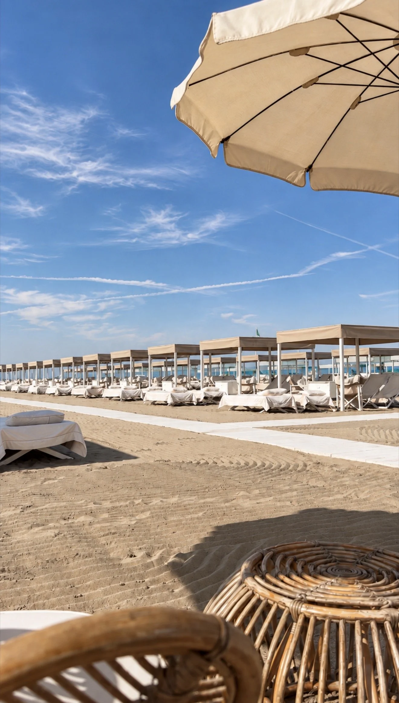 Private sandy beach lined with elegant cabanas and sun loungers beneath a clear blue sky