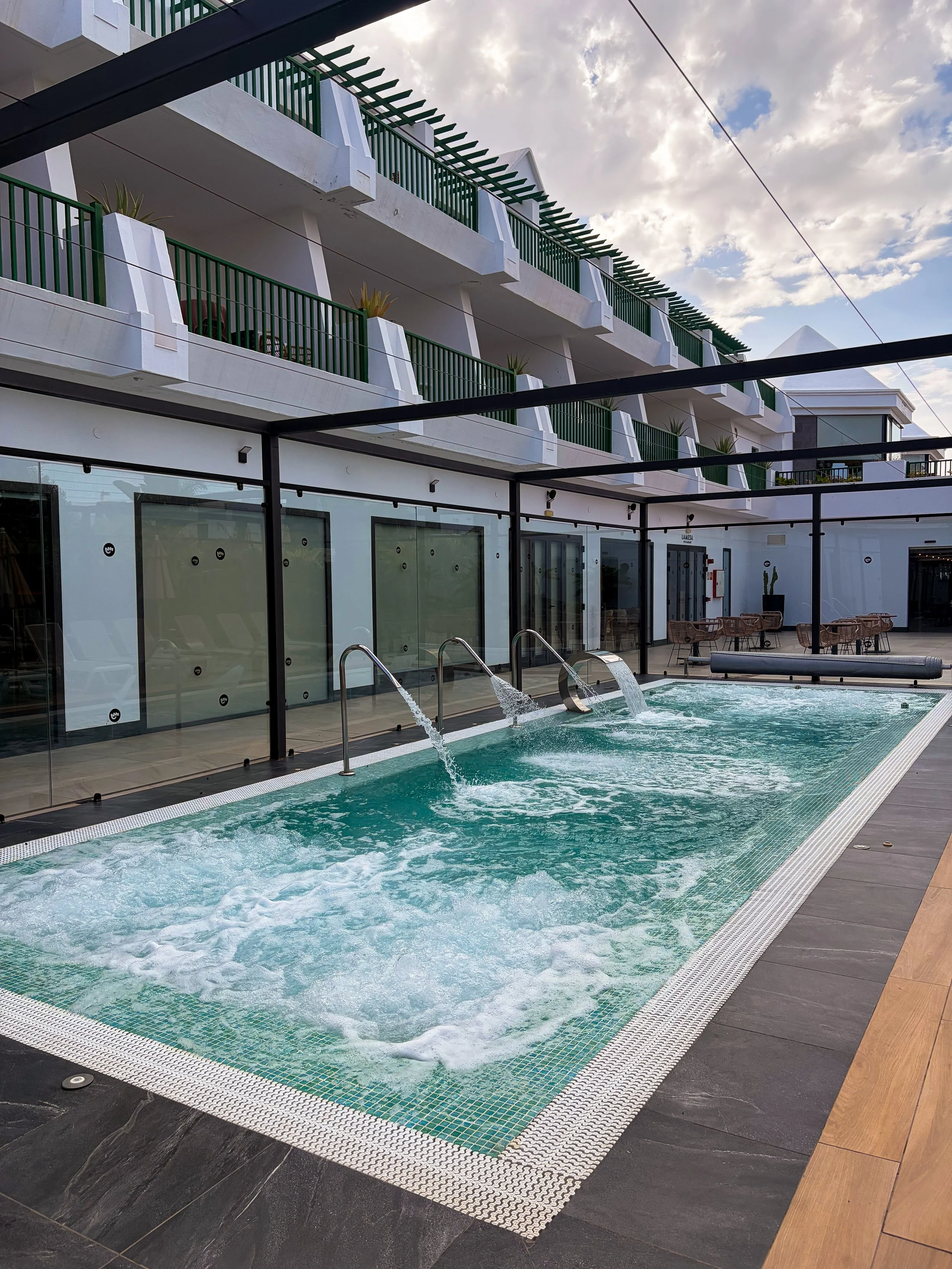 Outdoor hydrotherapy pool with bubbling water jets, modern glass walls, and surrounding guest room balconies
