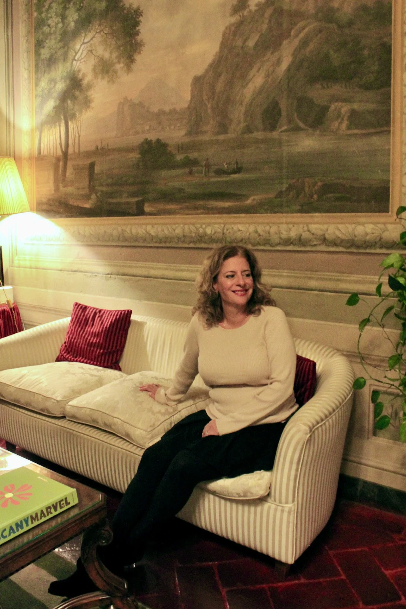 Guest relaxing on striped sofa beneath classical landscape mural in historic lounge, Palazzo Niccolini al Duomo – Florence, Italy.