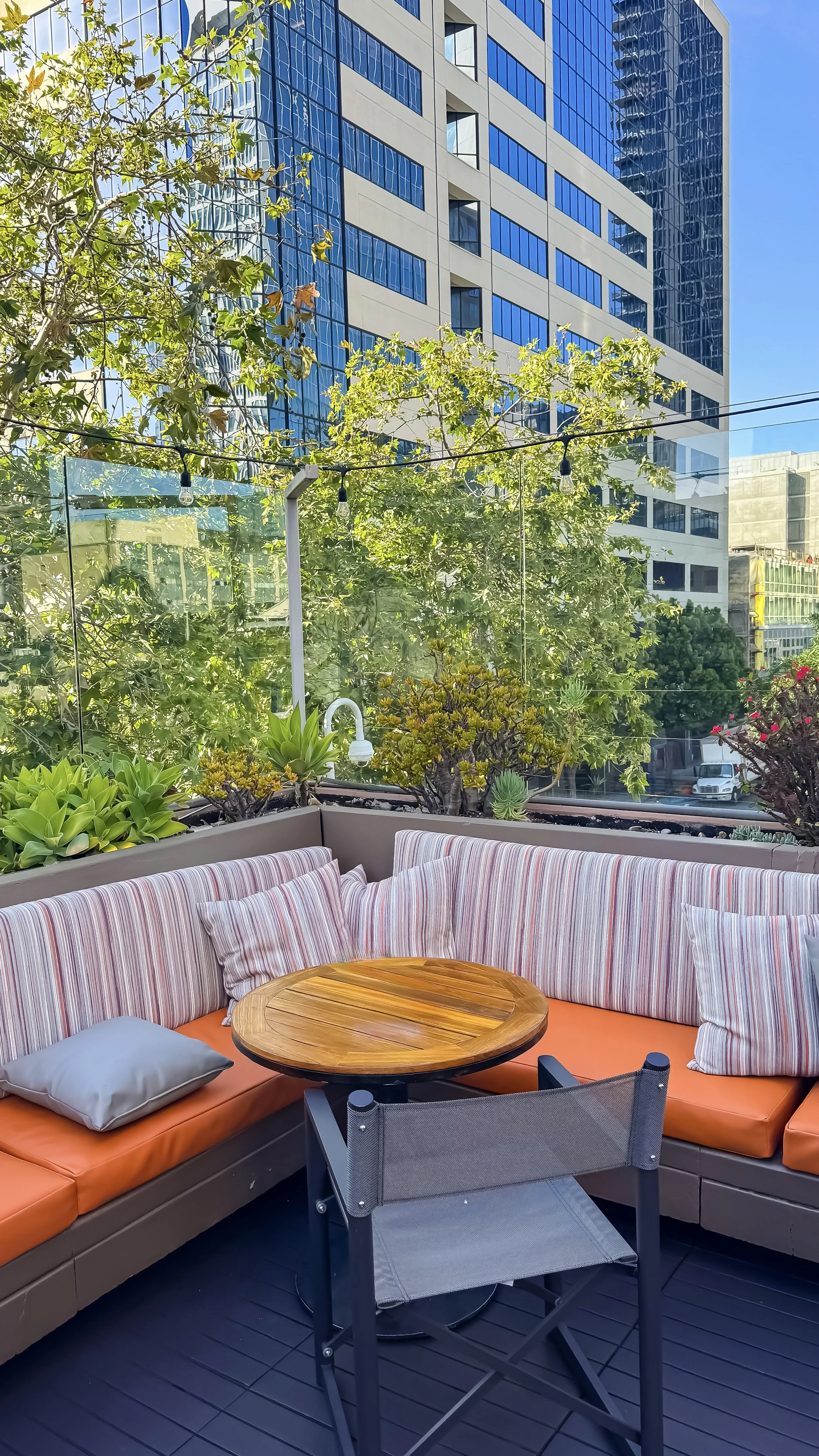 Rooftop terrace seating with striped cushions, wooden tables, and lush greenery overlooking the city skyline, Hotel Republic San Diego – San Diego, California.