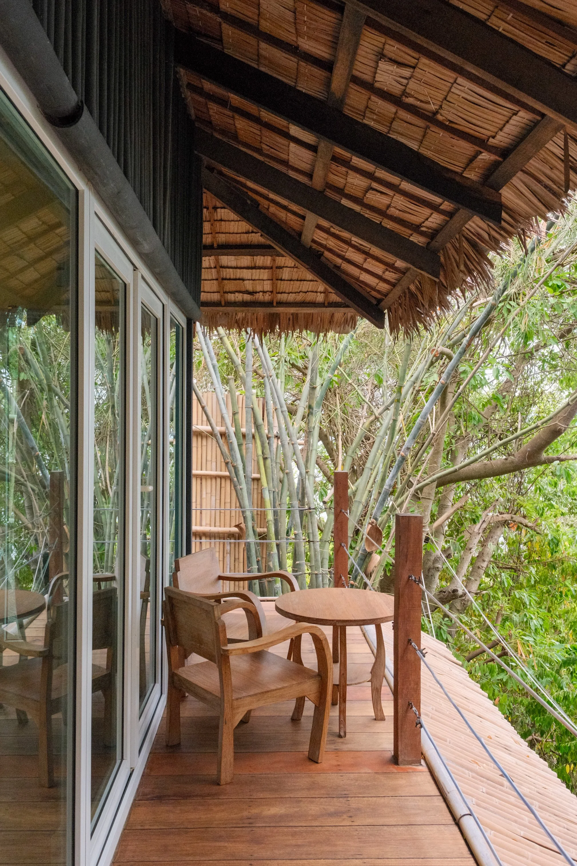 Private wooden villa terrace with simple seating beneath a thatched roof and bamboo surrounded by tropical foliage