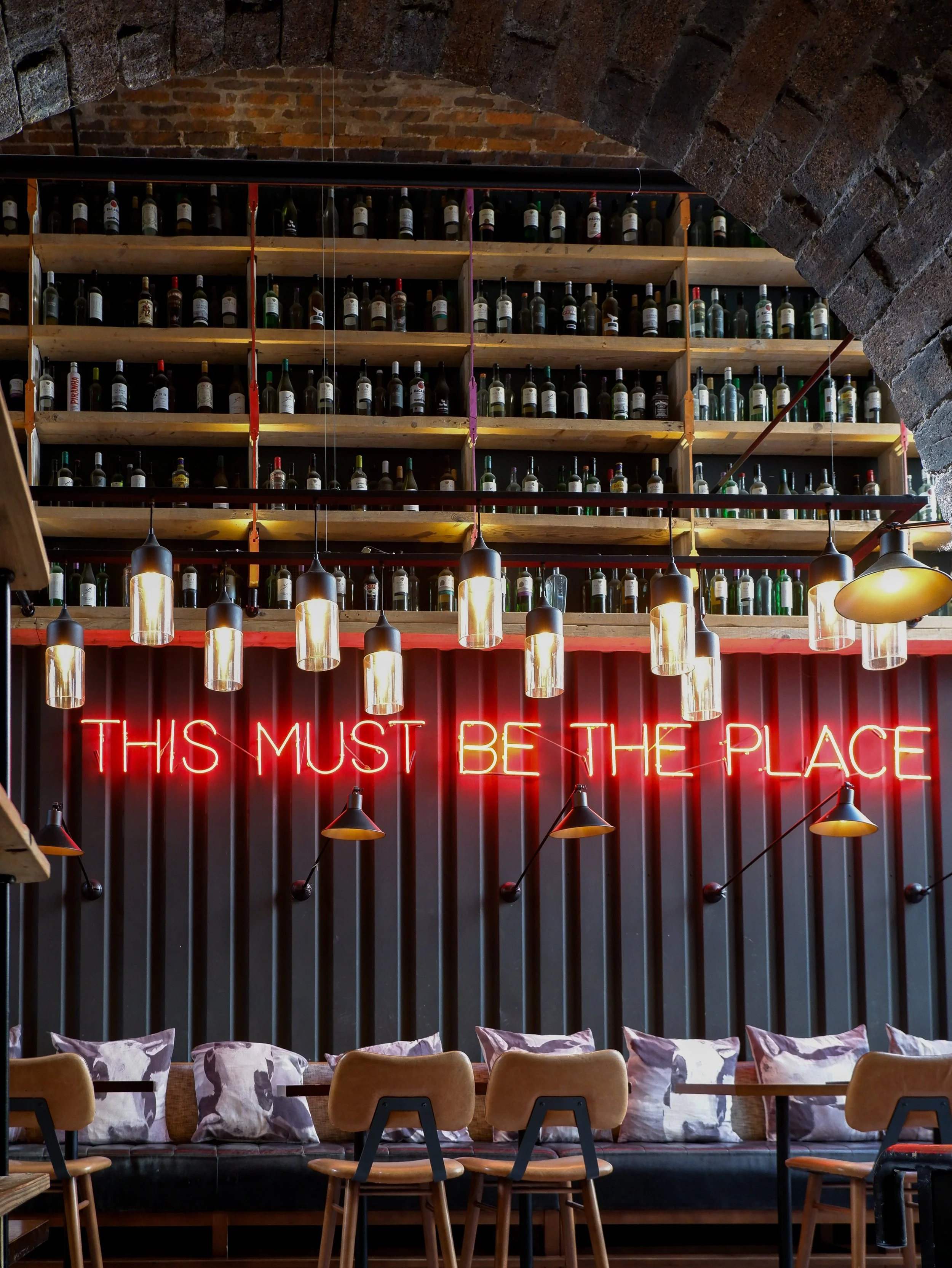 Stylish restaurant interior featuring a red neon sign, hanging pendant lights, and shelves filled with bottles