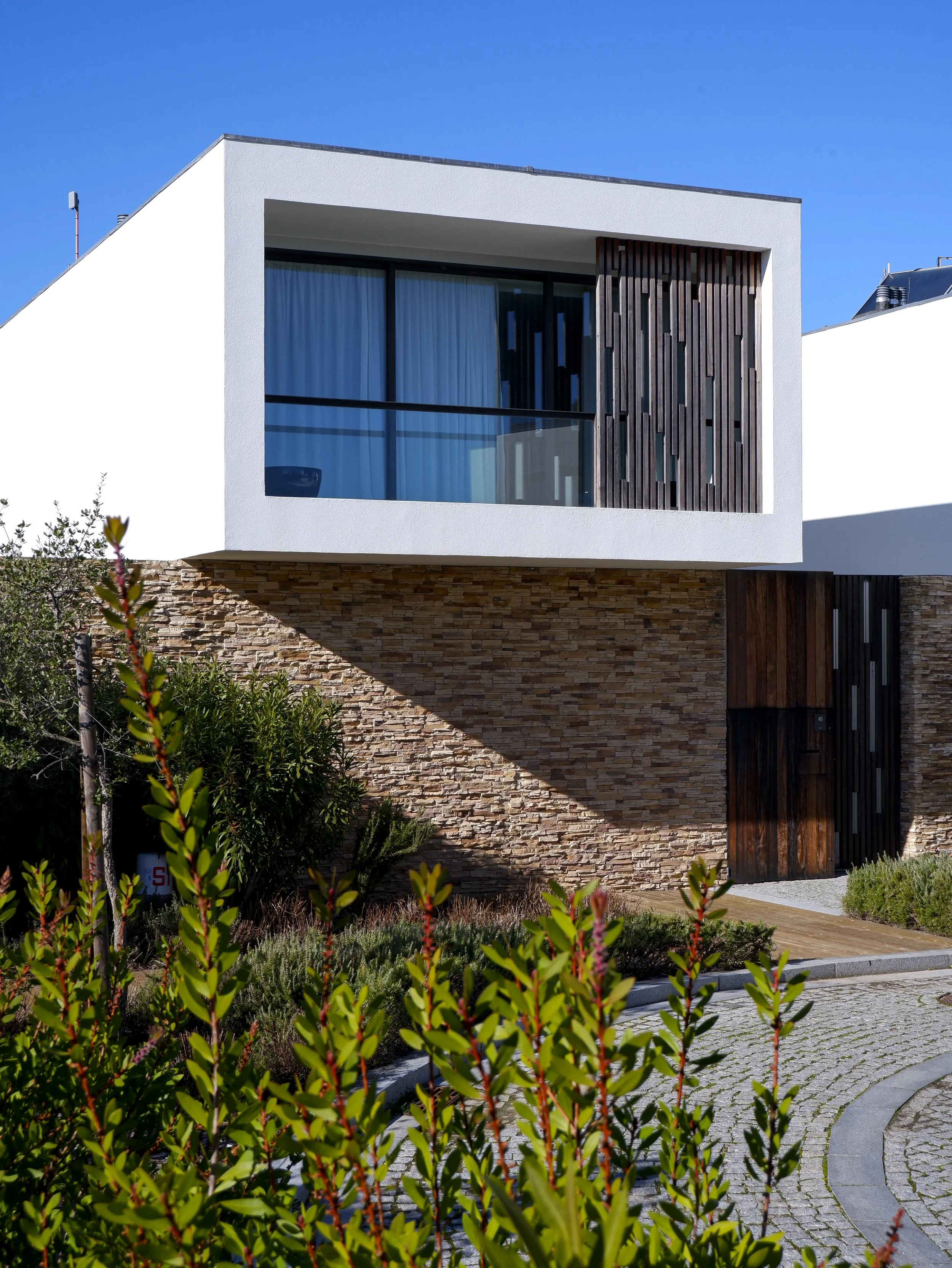 Modern villa façade combining white volumes, stone walls, and wooden screens integrated into the landscape — Octant Évora