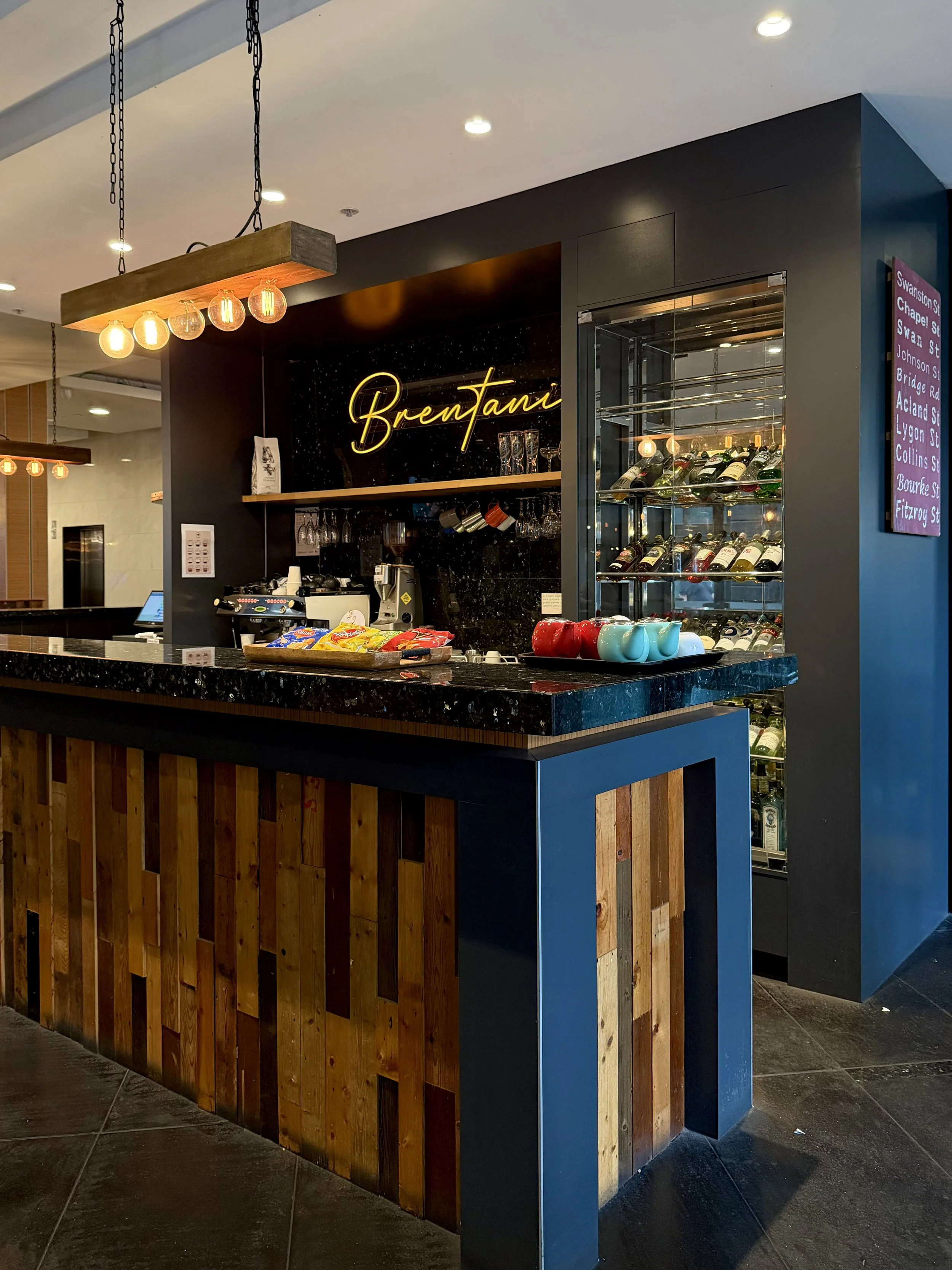 Modern hotel bar featuring a black marble counter, wooden panels, hanging lights, and a glass wine display