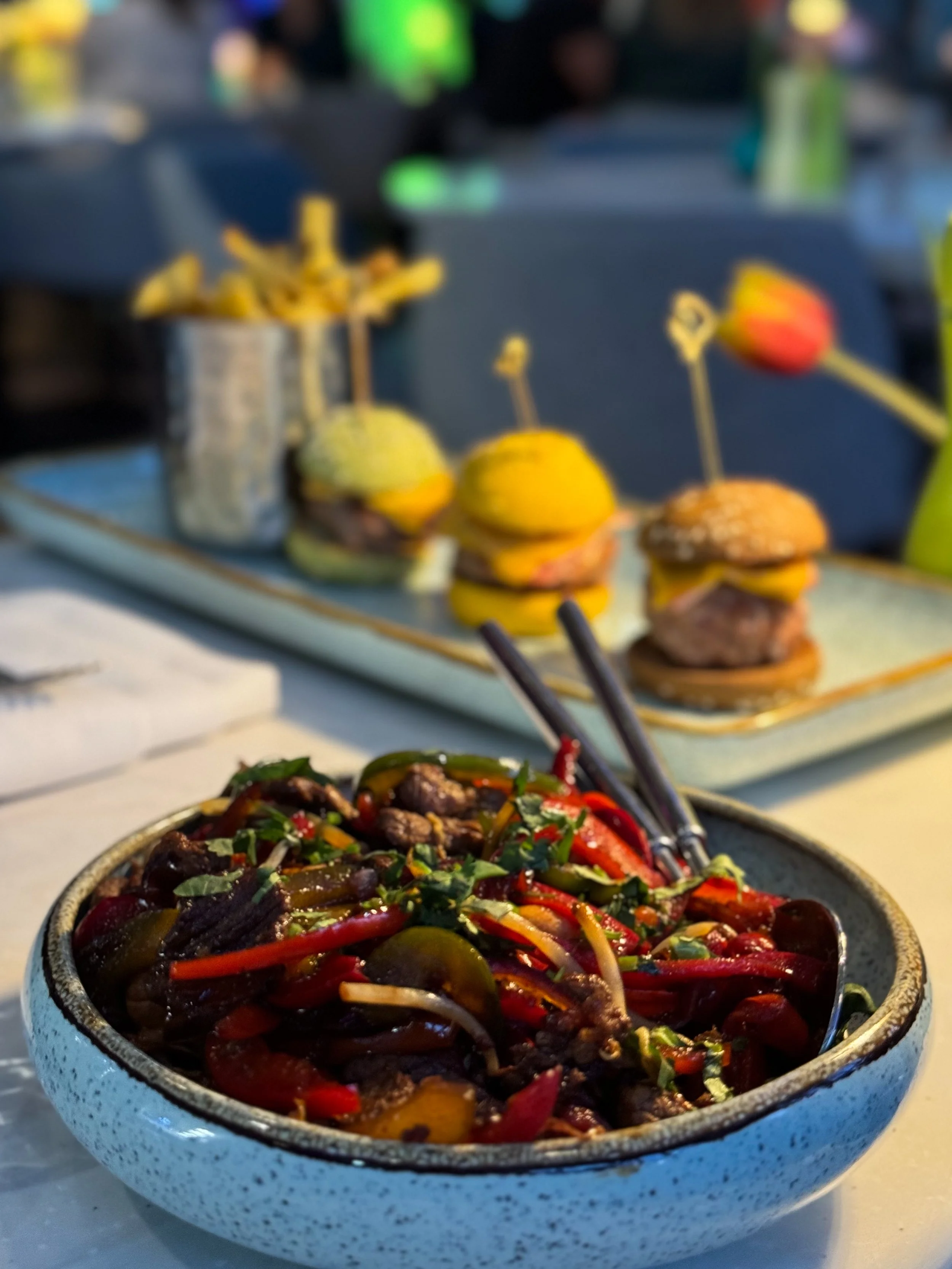 Vibrant dining scene featuring gourmet dishes and sliders in a lively outdoor setting, showcasing modern cuisine, Martinhal Lisbon Oriente – Lisbon, Portugal.