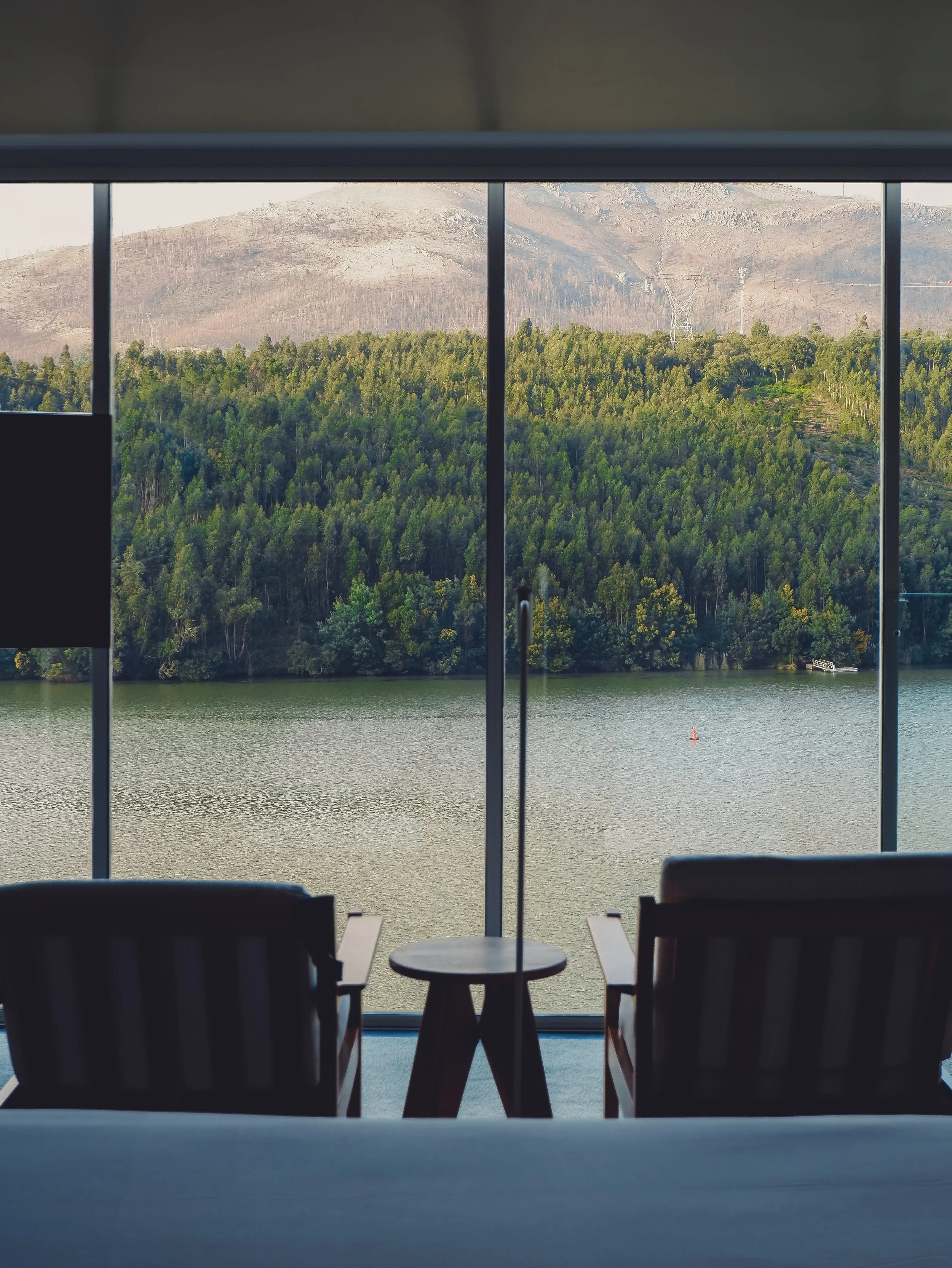 Serene seating area facing expansive river and forest views through large windows, designed for relaxation and connection to nature, Octant Douro – Castelo de Paiva, Portugal.