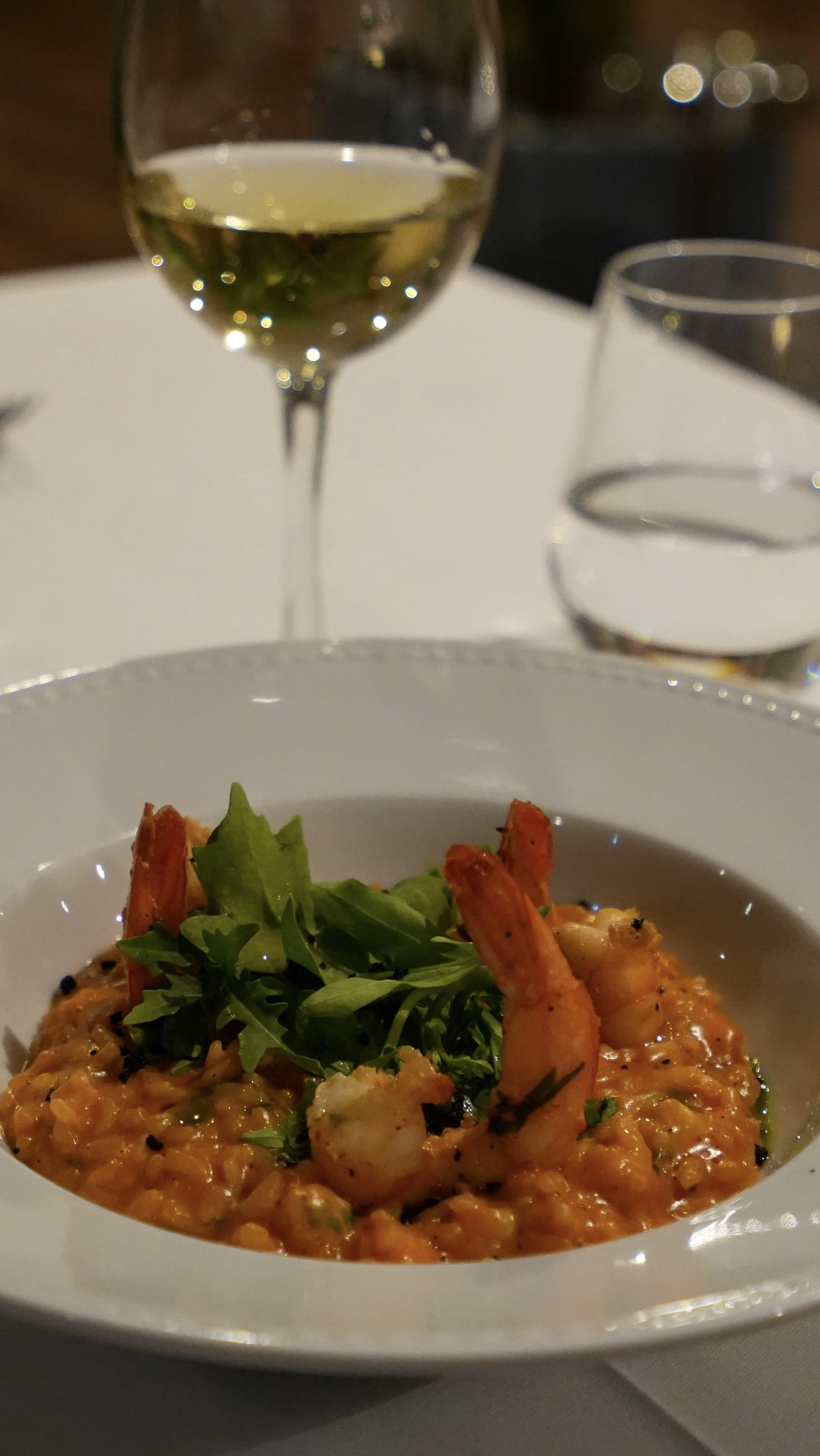 Creamy prawn risotto garnished with fresh greens, served alongside a glass of white wine