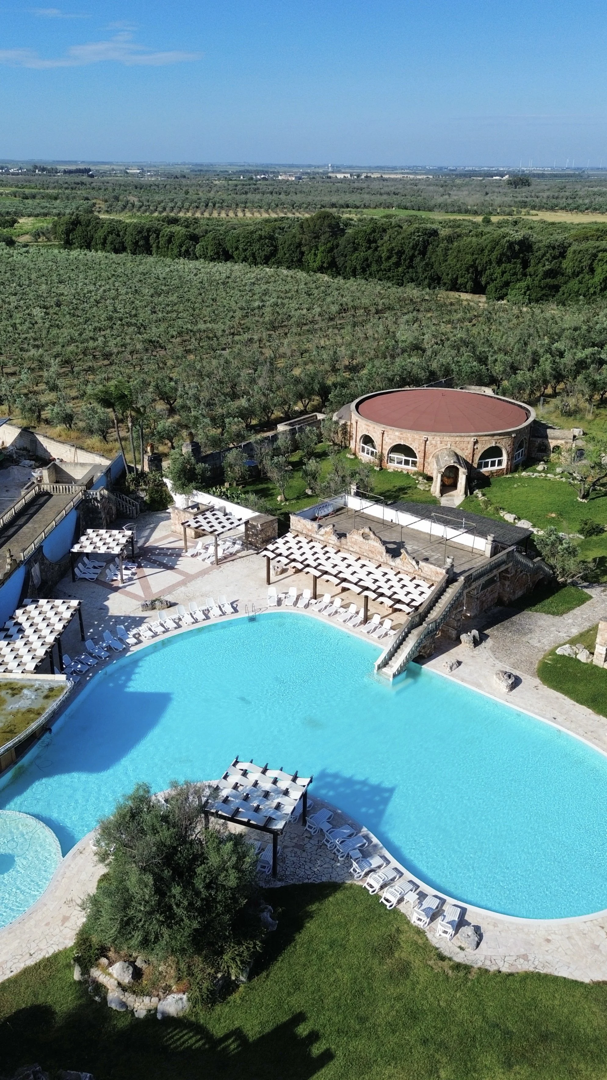 Aerial view of the resort’s lagoon-style swimming pool surrounded by olive groves and Mediterranean landscapes at Tenute Al Bano