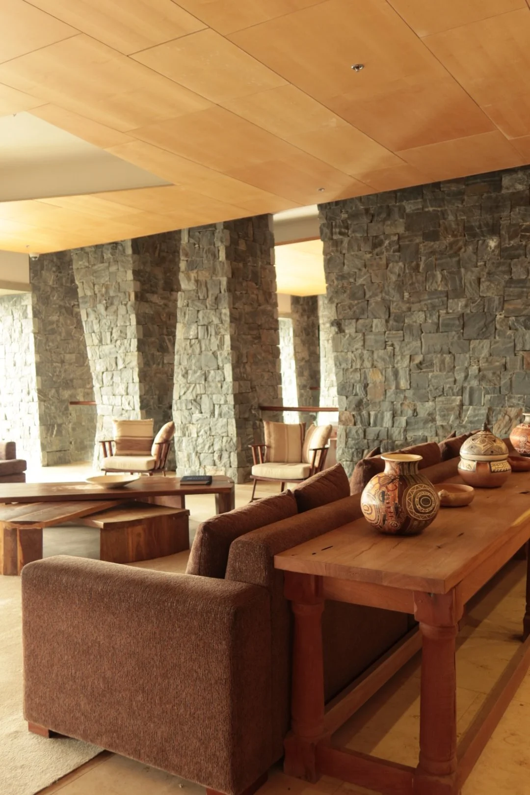 Spacious lounge with natural stone walls, warm wood furnishings, comfortable seating, and handcrafted ceramics