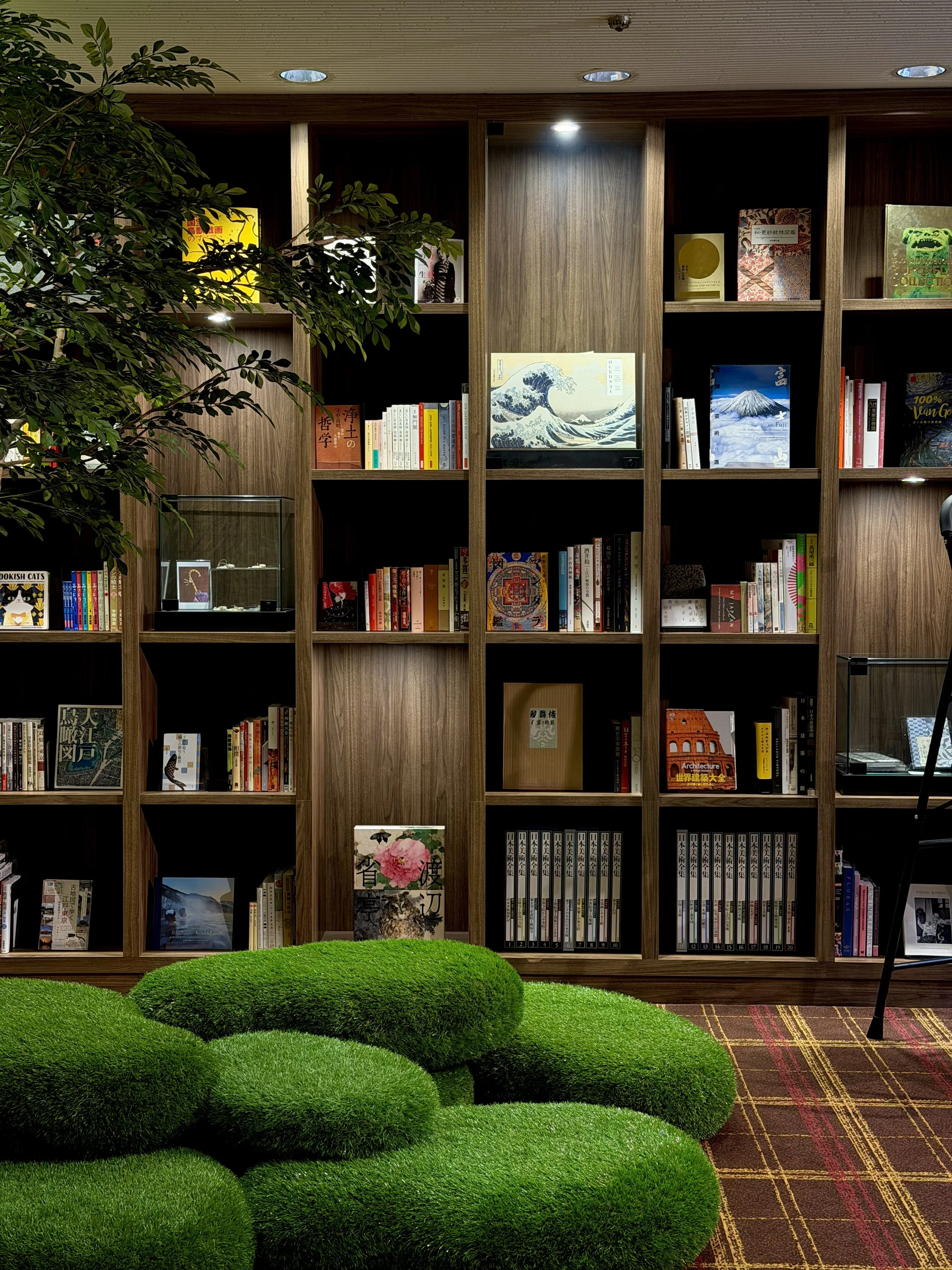 Japanese-inspired library with curated bookshelves, indoor greenery, and sculptural green seating