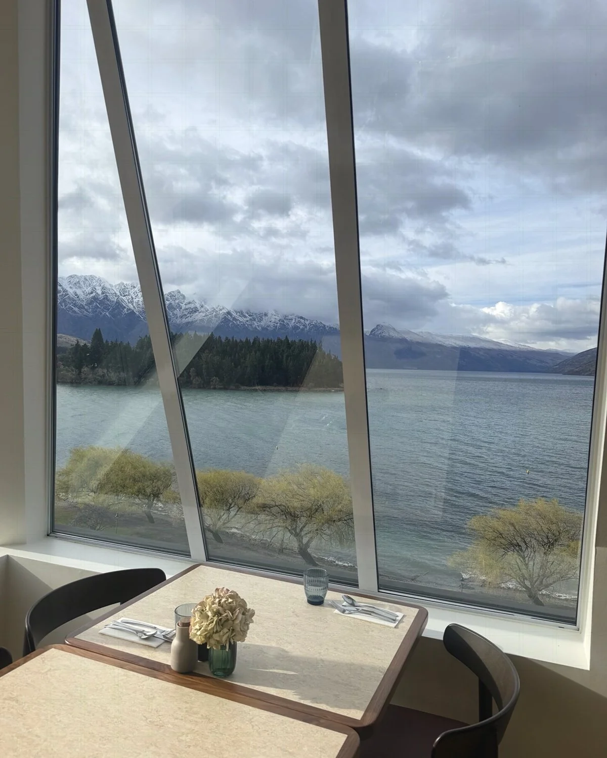 Restaurant dining area with floor-to-ceiling windows offering panoramic views of Lake Wakatipu and snow-capped mountains