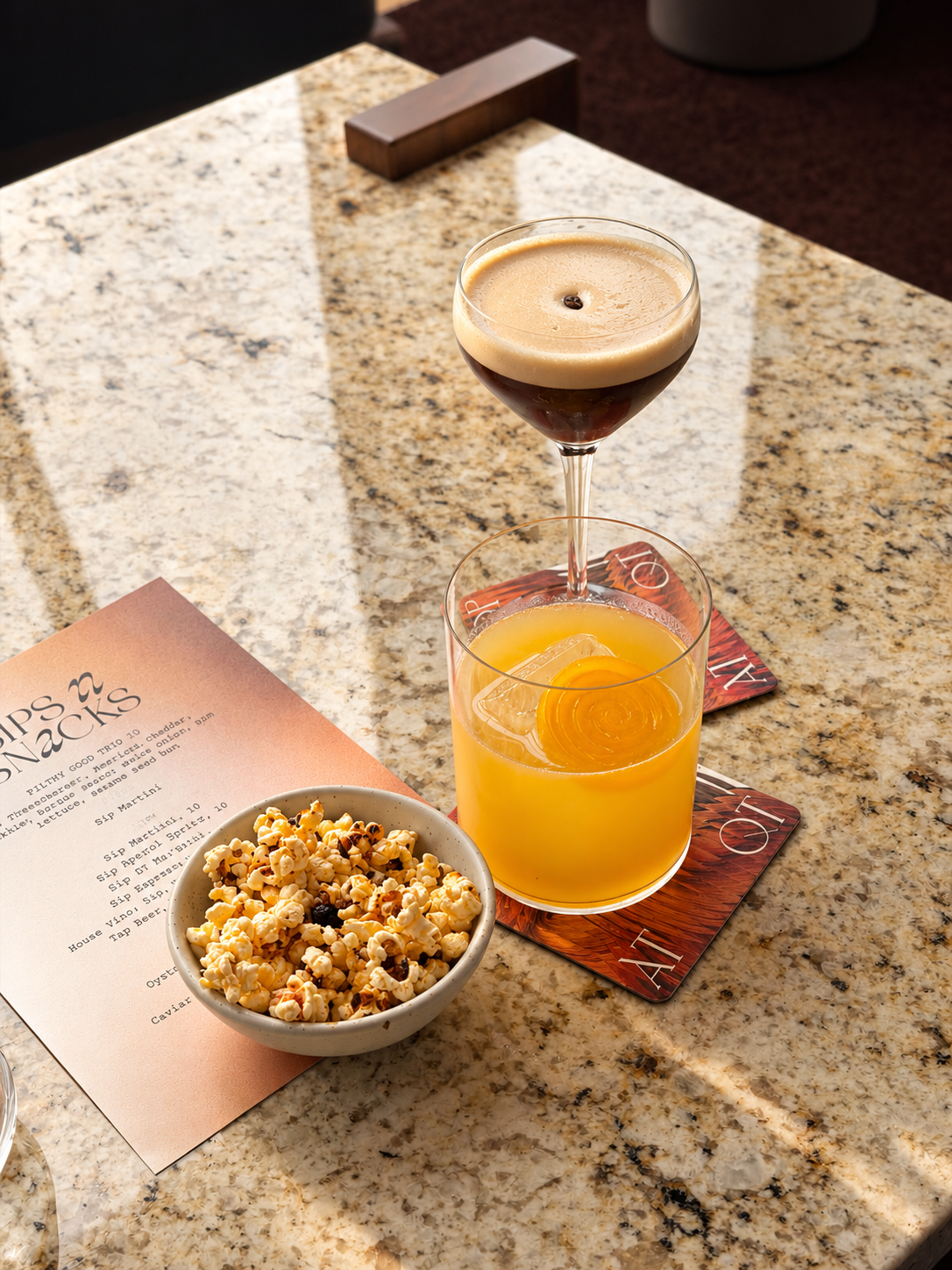 Espresso martini and orange cocktail served with a bowl of popcorn on a marble table